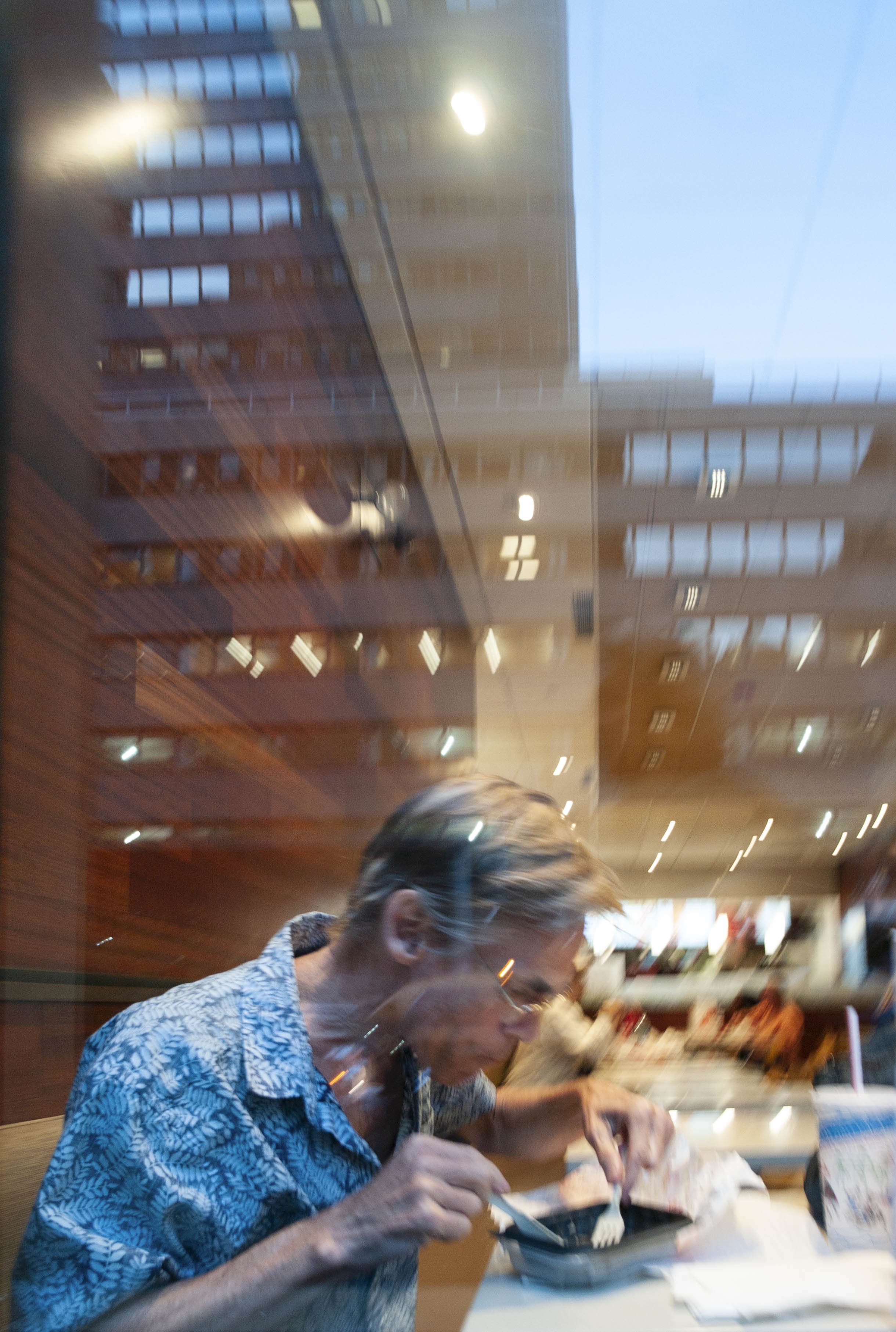 People dining at a restaurant, focus on a woman with short hair wearing a patterned shirt, eating with utensils at a table.