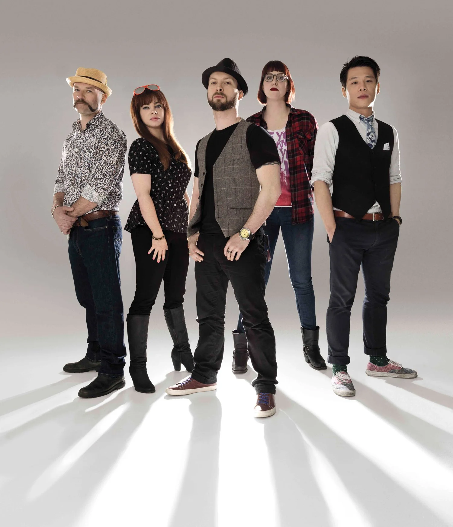 Backlit image of five bartenders on a neutral background projecting long shadows into the foreground. From left, the first figure is male with a black and white patterned shirt, jeans, and a straw hat. next to him is a young woman dressed in black, f