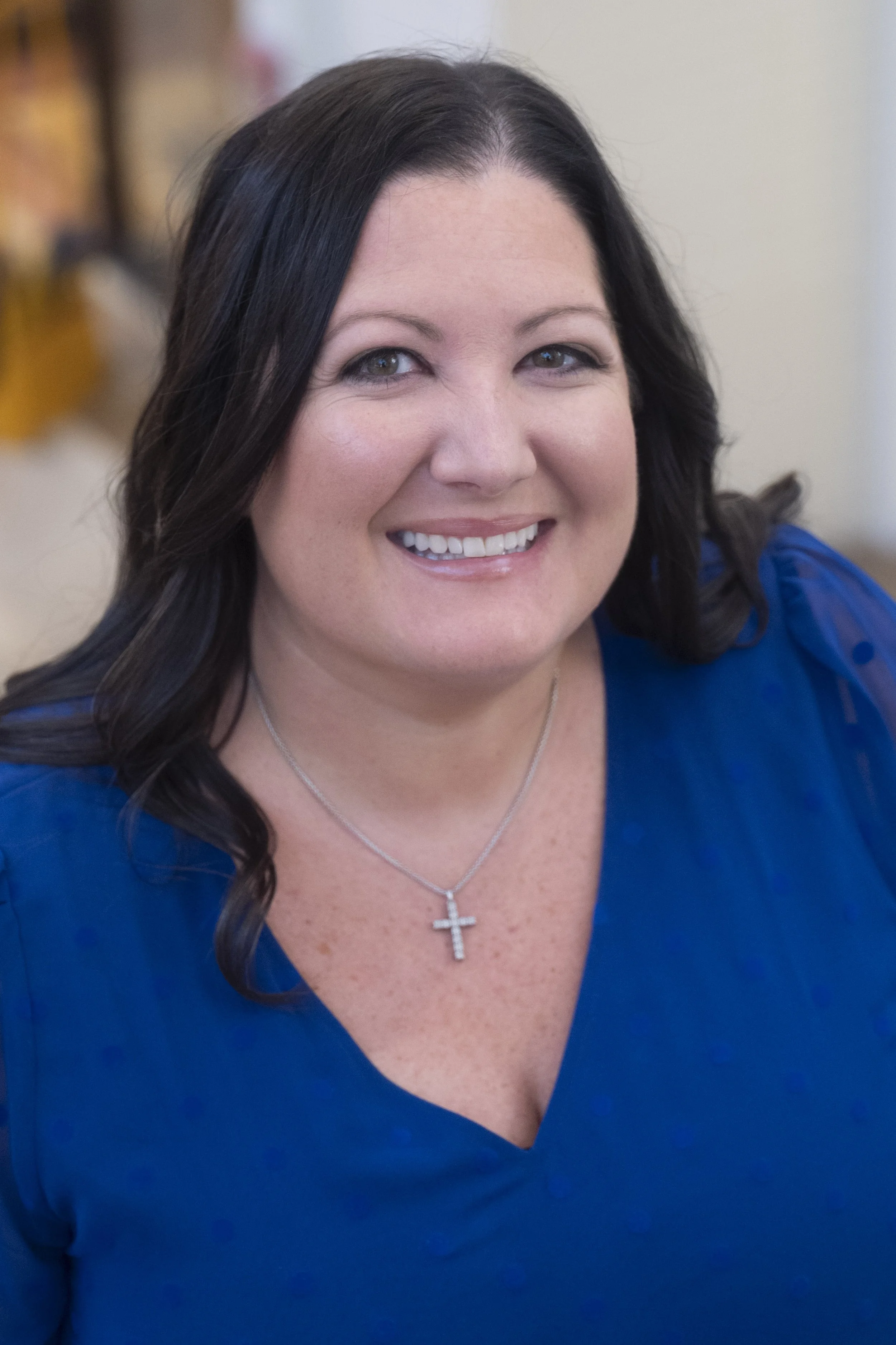 Smiling woman with long, dark hair, in a bright blue dress smiles for a candid portrait.