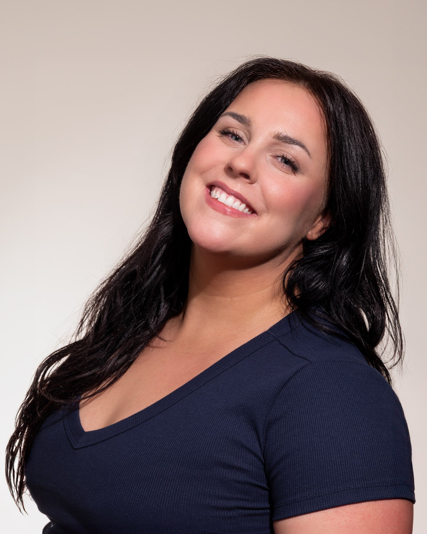 A woman with long dark hair smiling and wearing a navy blue top.