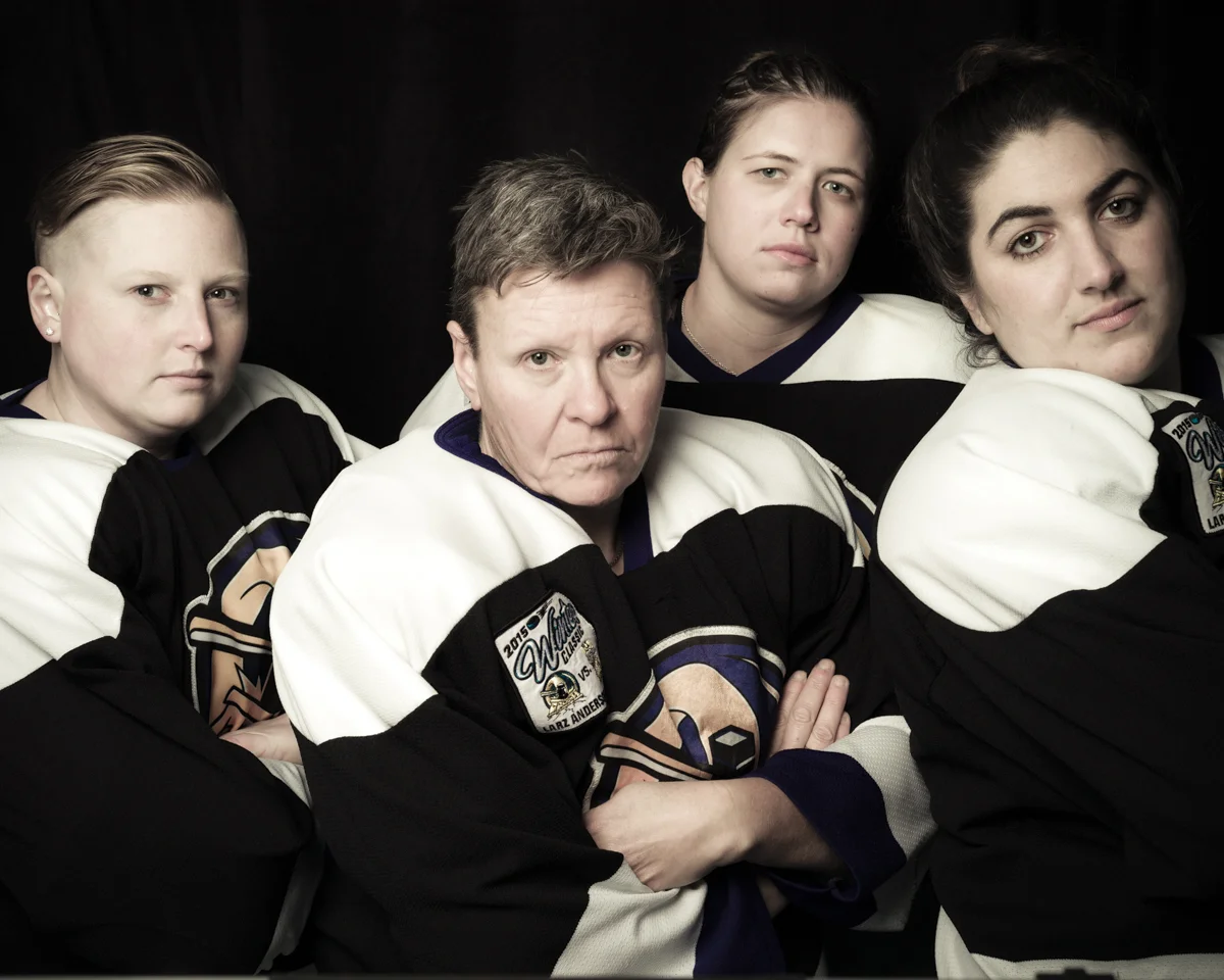 Group photo of four female hockey players in black and white uniforms on a black background, cropped waist-level.