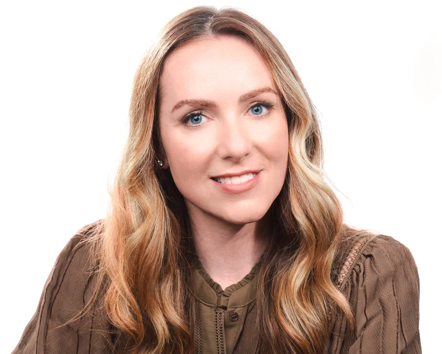 Headshot of a woman with long, wavy blonde hair, blue eyes, and fair skin, wearing a brown top against a white background.