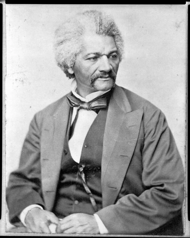 Studio portrait of abolitionist Frederick Douglass, seated in formal attire of the period, looking off-camera.