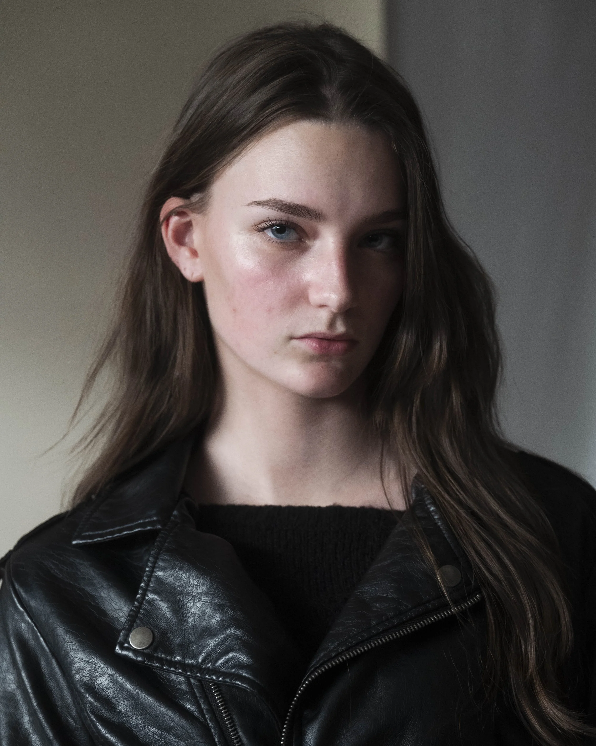 Portrait of a young woman with long brown hair, blue eyes, and fair skin, wearing a black leather jacket.