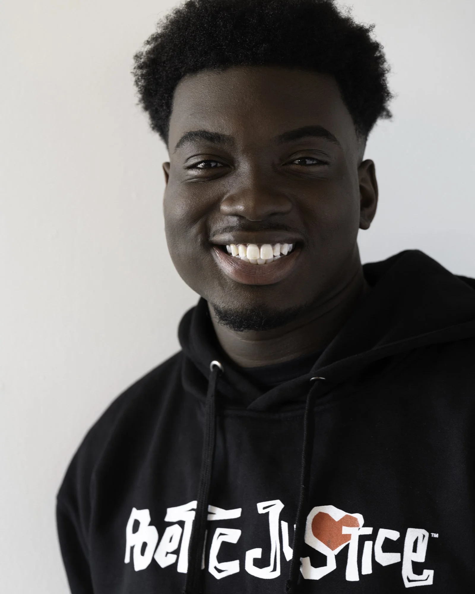 Young, smiling Black man in a black hoodie displaying Poetic Justice movie graphics in white and red across his chest.