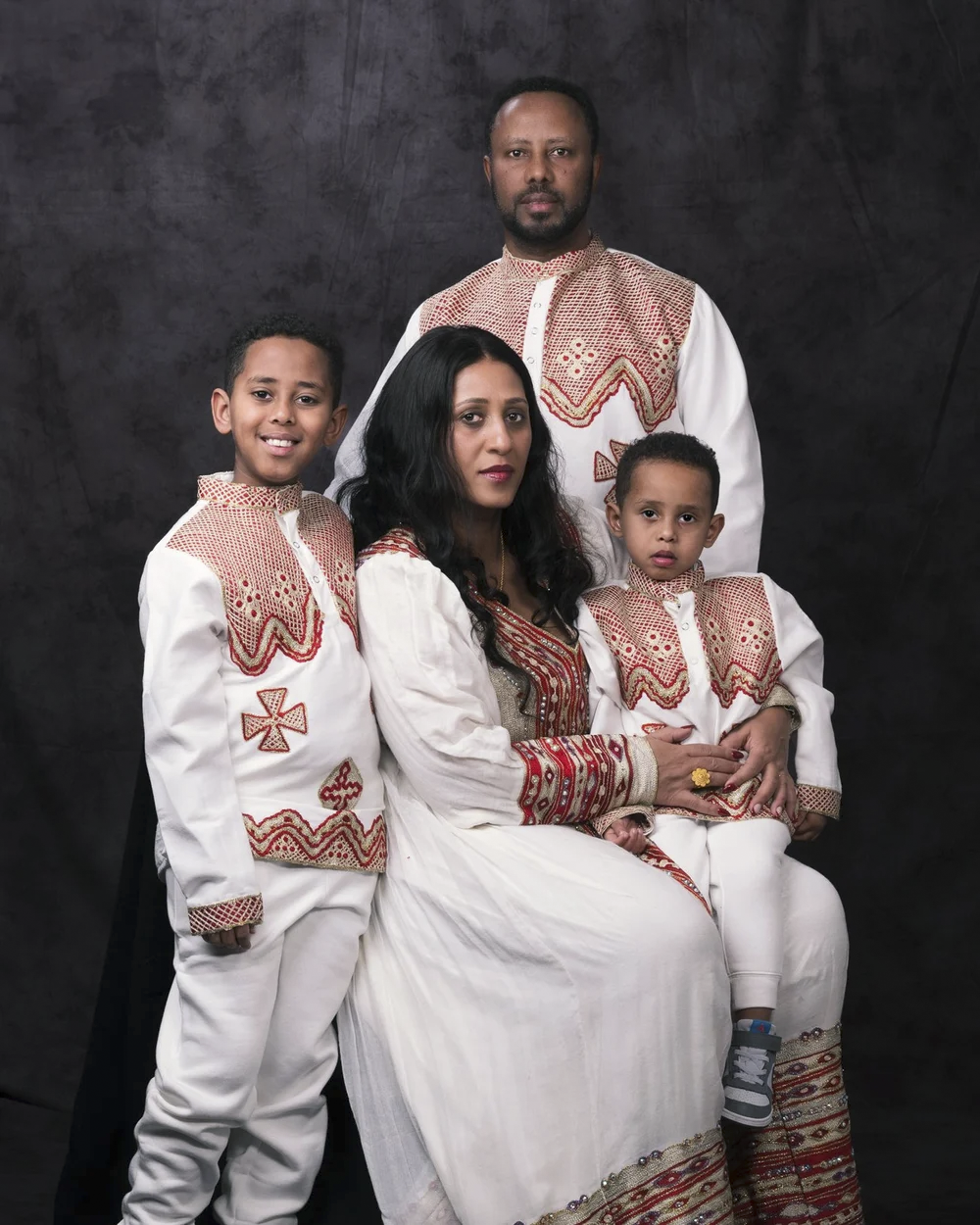 A family of five dressed in traditional red and white Ethiopian attire, posing for a portrait against a dark background.