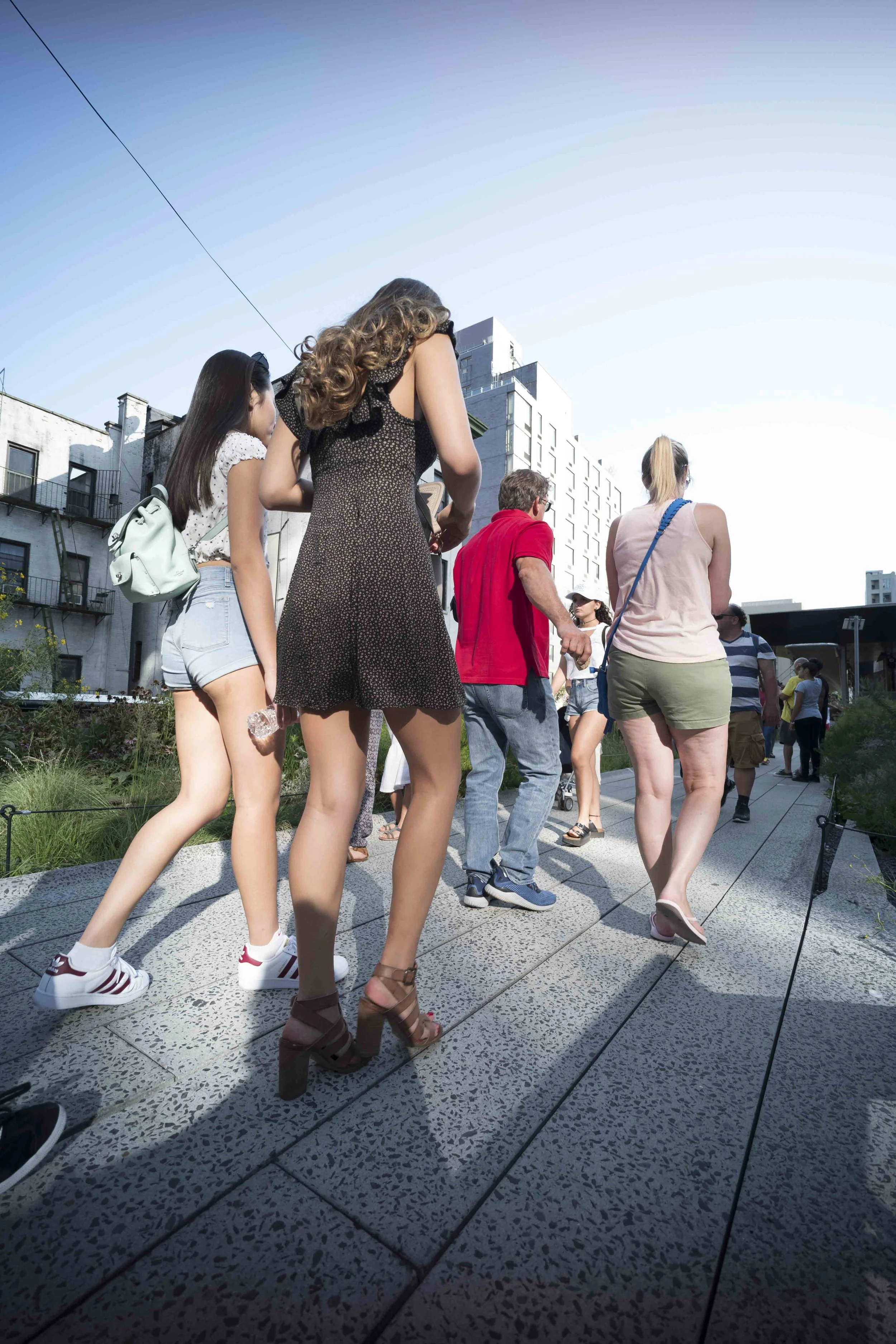 Group of people walking outdoors on a sunny day in an urban area, with modern buildings in the background.