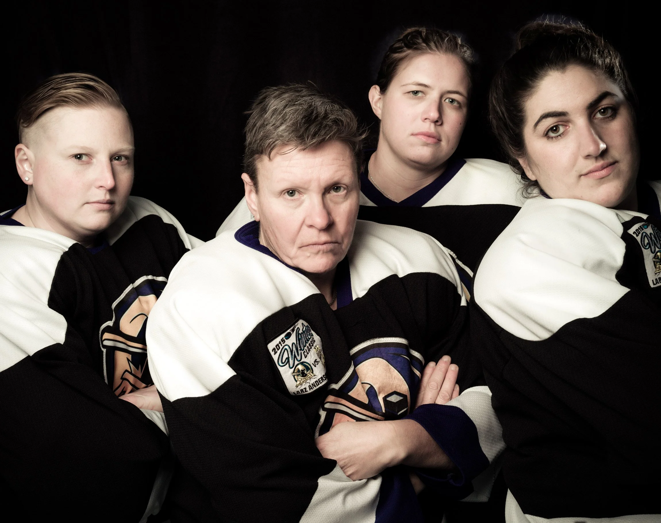 Four team members of Boston Crush, a women's hockey squad based on Boston's South Shore. Photographed in their black and white uniforms against a black background.