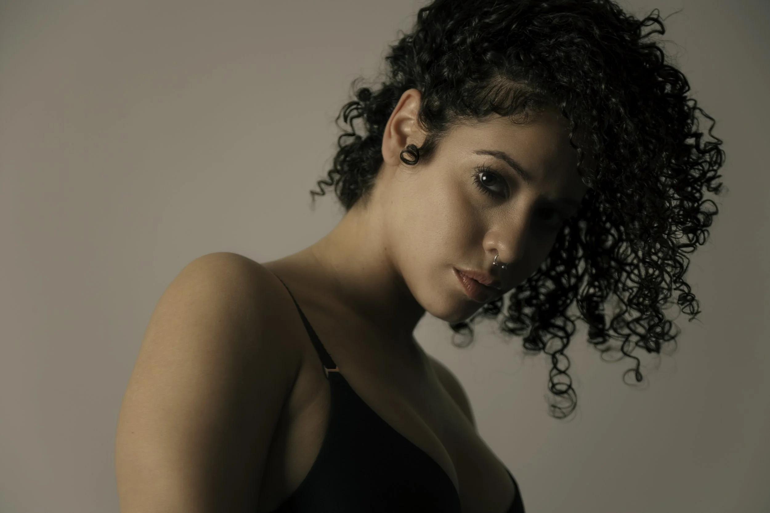 A portrait of a woman with short curly black hair, wearing a black tank top, with a neutral background.