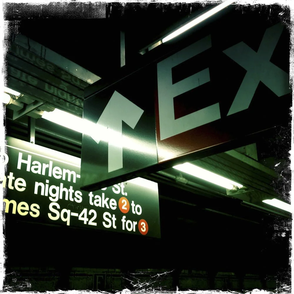 An underground subway station with illuminated signs. A large black sign with white and red letters shows directions for the subway, with a bright 
