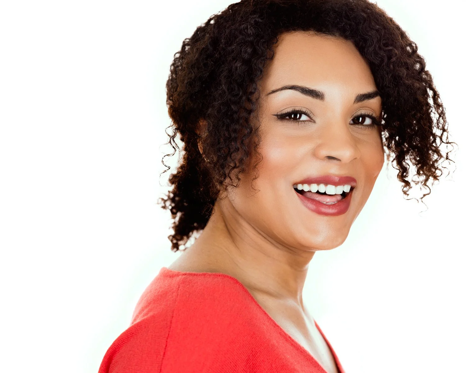 Smiling woman with curly hair wearing a red top against a white background.