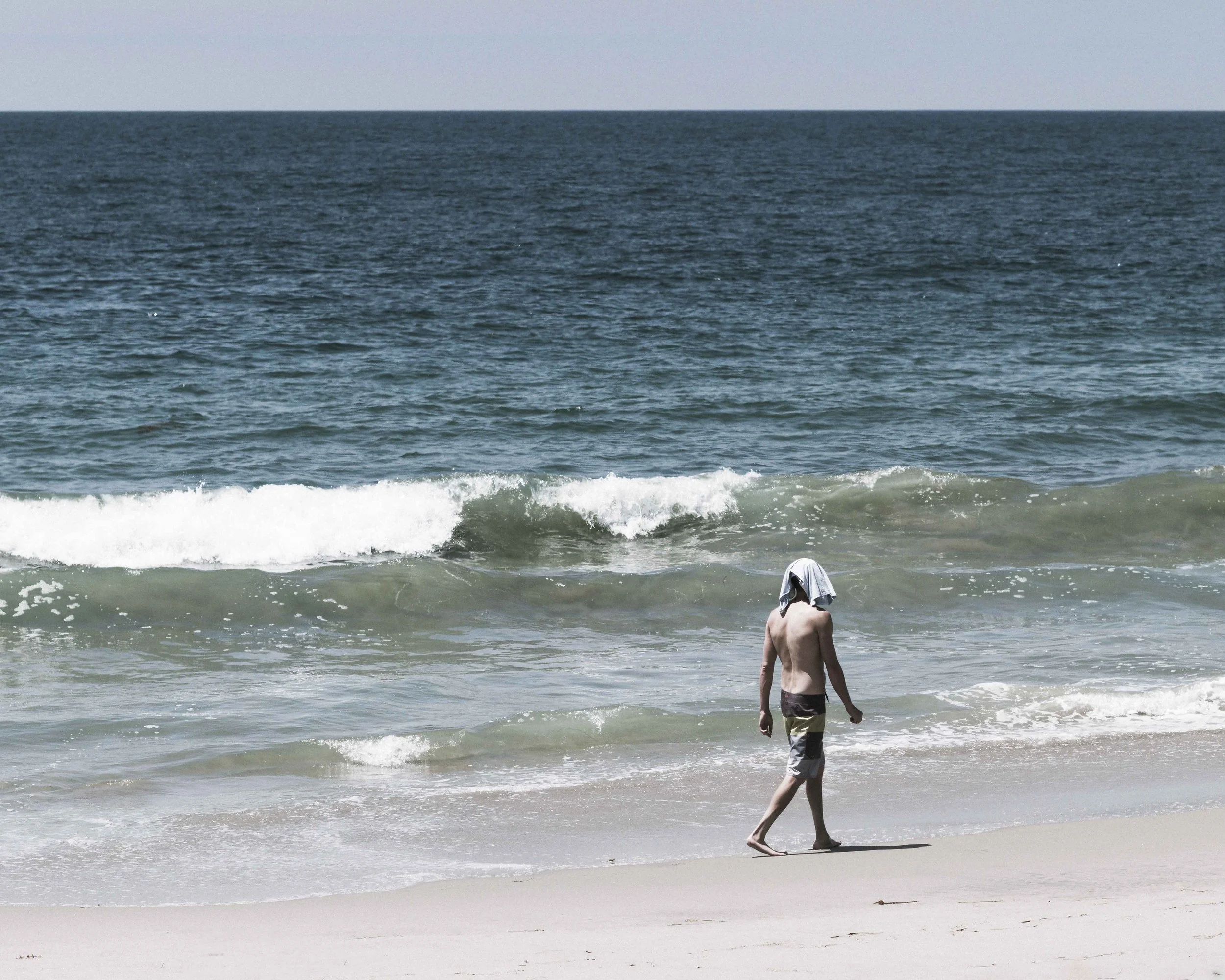 A person walking on the sandy beach near the shoreline with waves crashing around them, at the ocean on a clear day.
