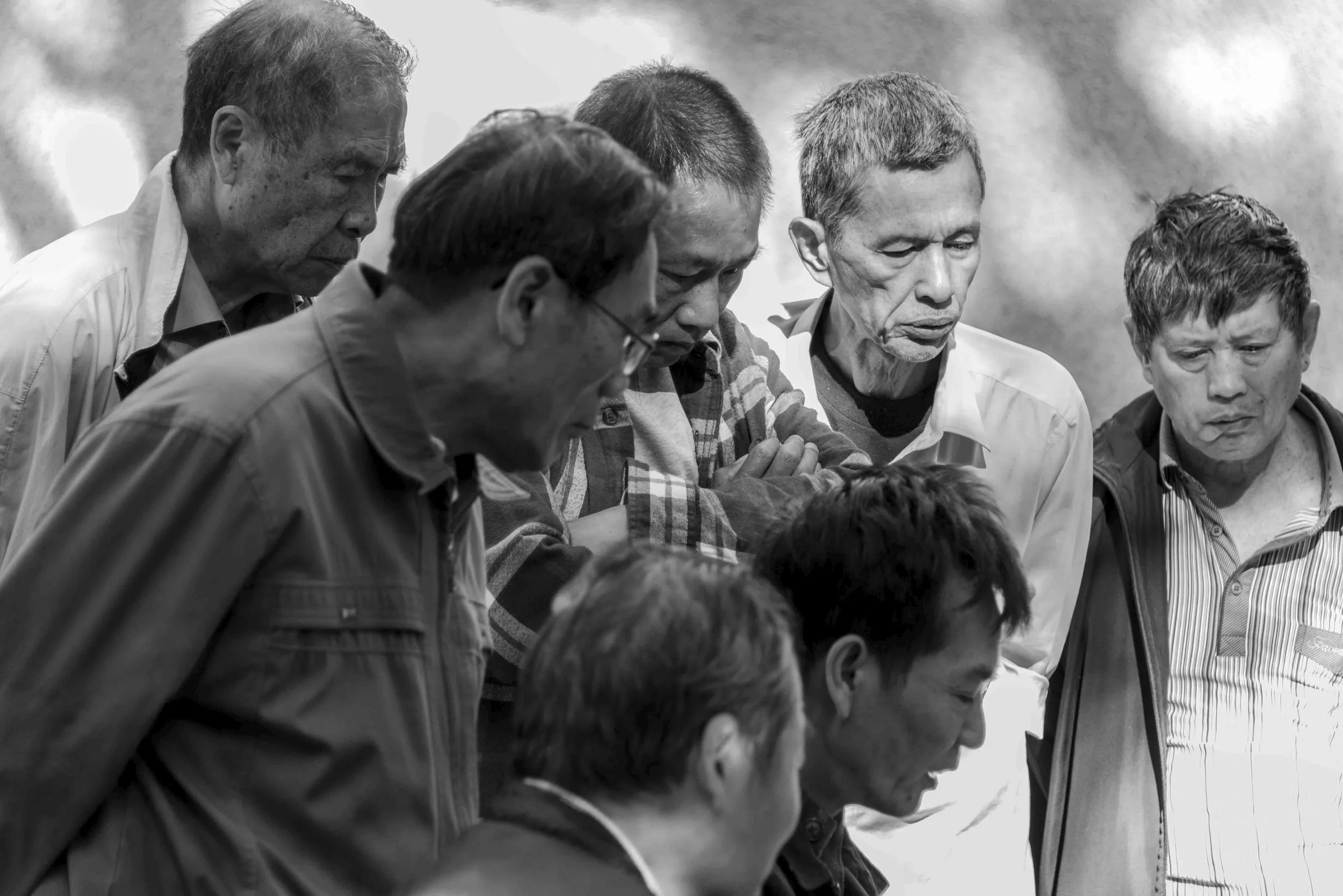 Black and white photo of a group of men with heads bowed, appearing to be in prayer or meditation.