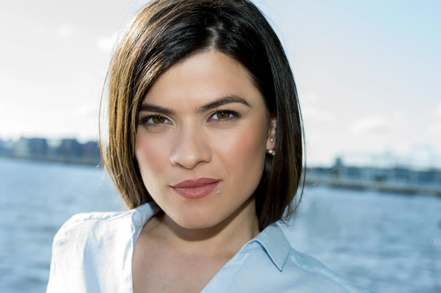 An outdoor portrait of young woman with dark with a body of water and horizon line in background. Mixed natural light with fill-flash results in even skin tone with defined shadow under the jawline.