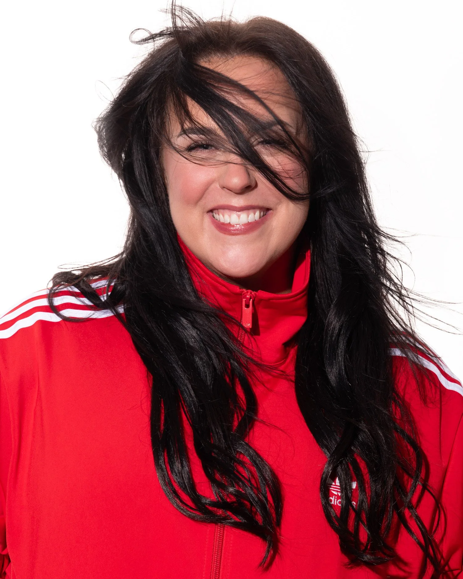 Smiling woman with long dark hair wearing a red sports jacket with white stripes on the shoulders.