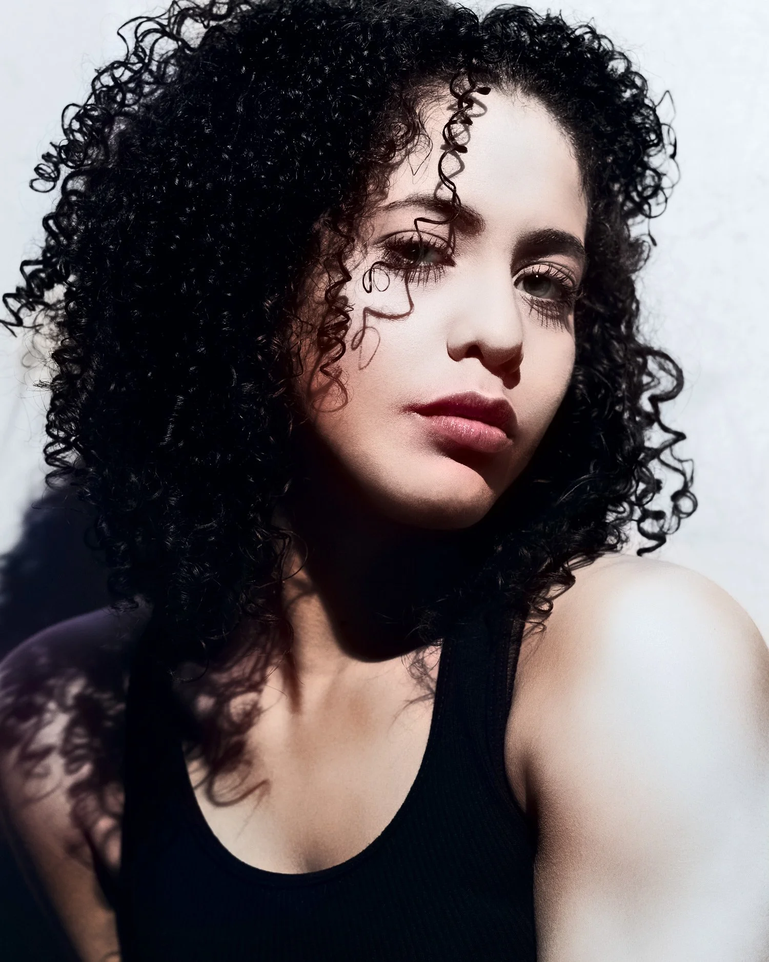 Portrait of young Latina with long, curly black hair in high-key lighting against a white background.