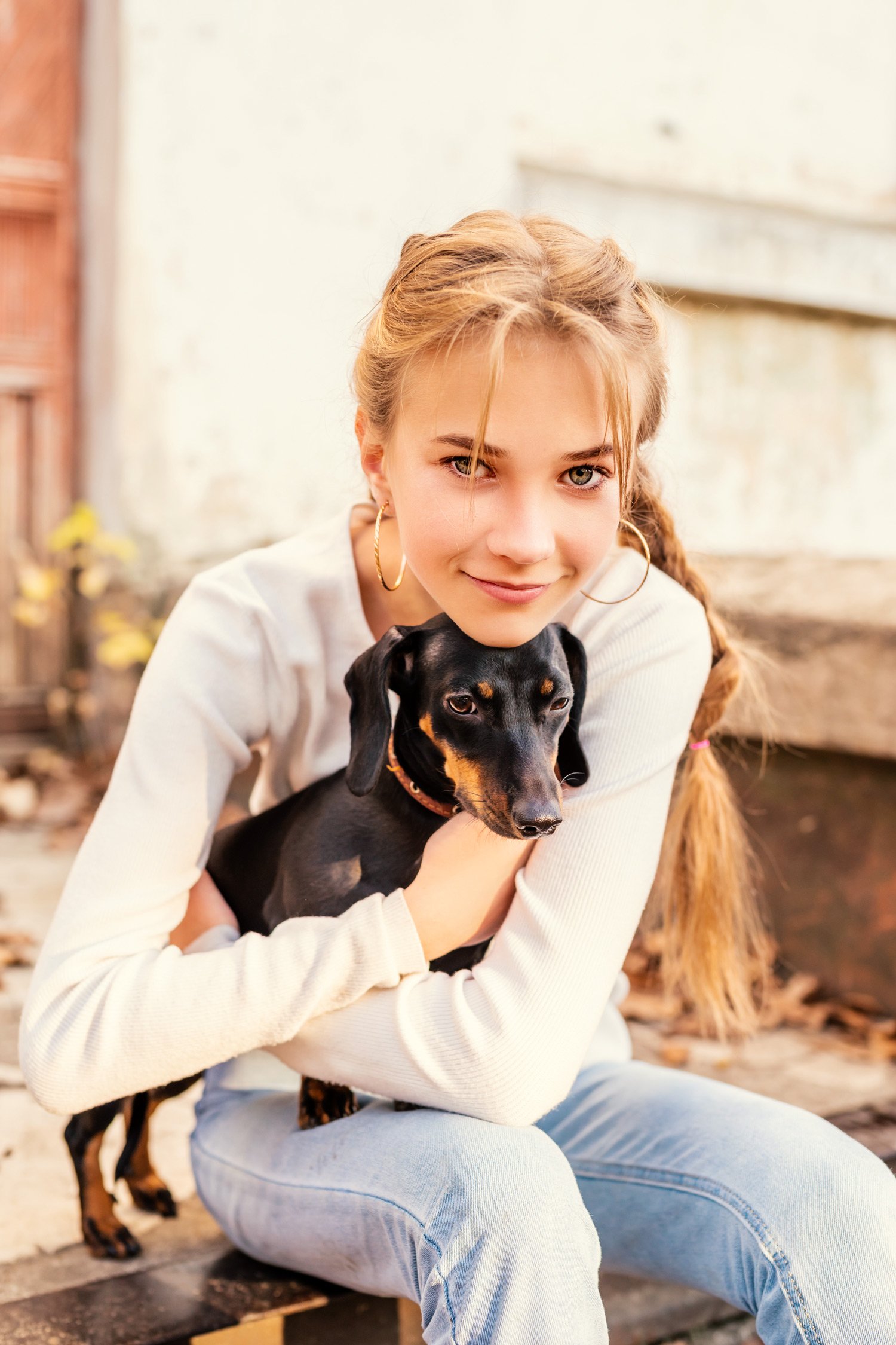 Young, blonde woman hugs her black and tan dachshund  dog in an outdoor setting with warm, natural light.