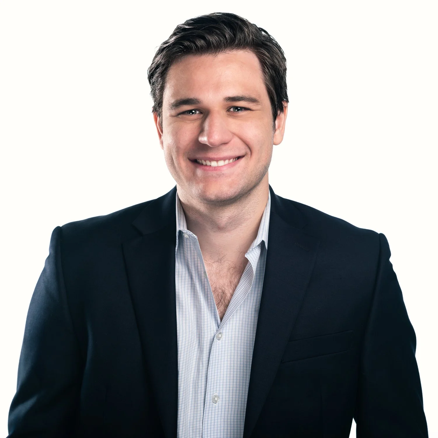 Portrait of a smiling man with dark hair, wearing a dark blazer and light dress shirt, against a plain white background.