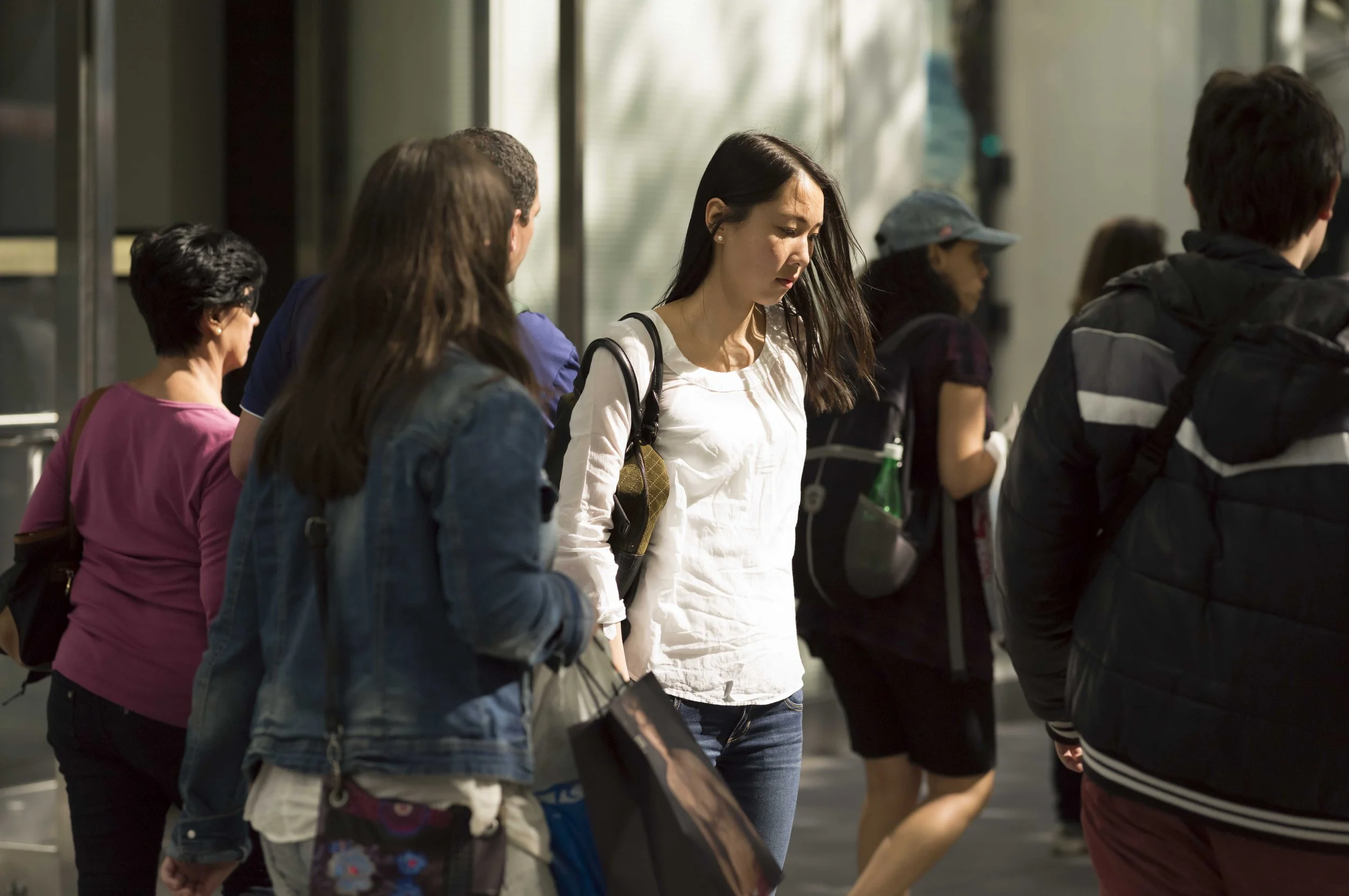 People standing in line inside a modern building, with a woman in a white shirt and dark hair looking down.