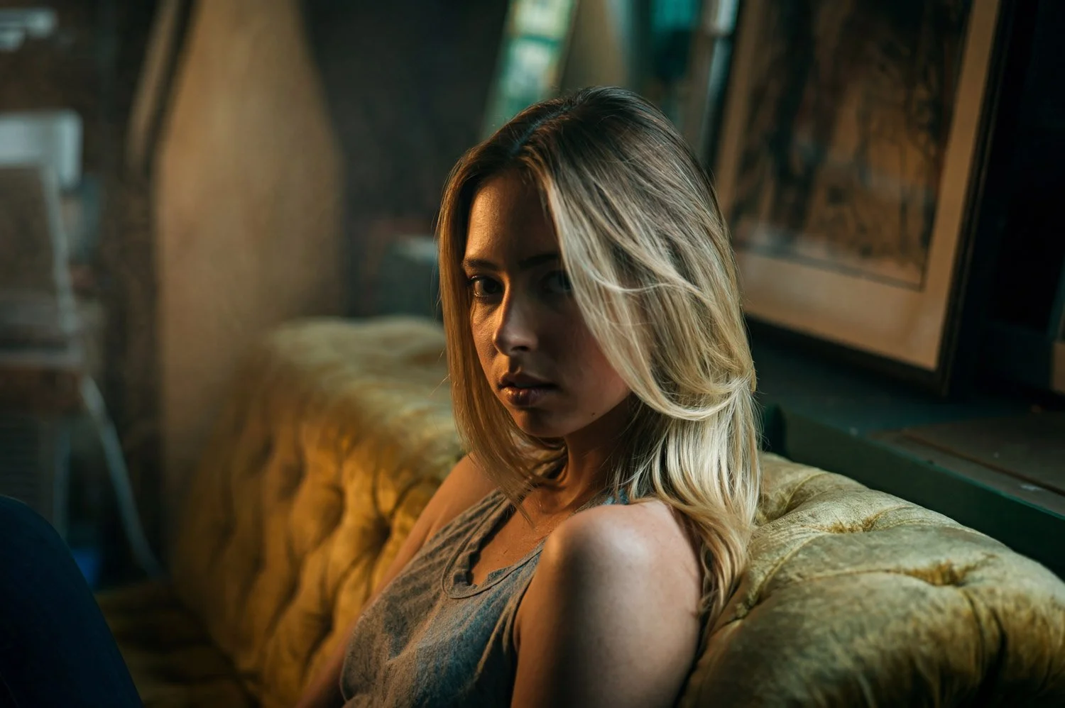 Young model with long, blonde hair seen in a screen test sitting on a sofa, her face lit with short, golden light turns to the camera in a dramatic scene.