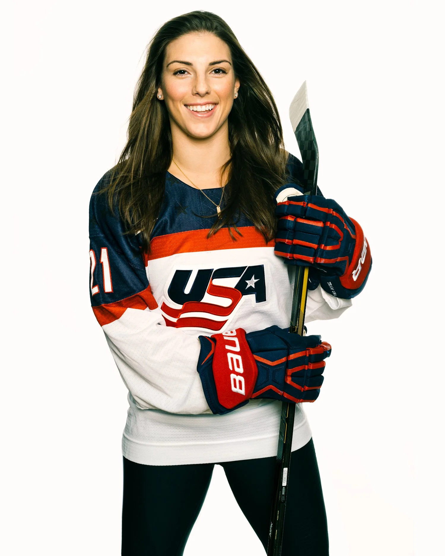 Olympic gold medalist Hilary Knight for The Improper Bostonian magazine cover wearing a USA hockey jersey and gloves, holding a hockey stick, smiling for the camera.