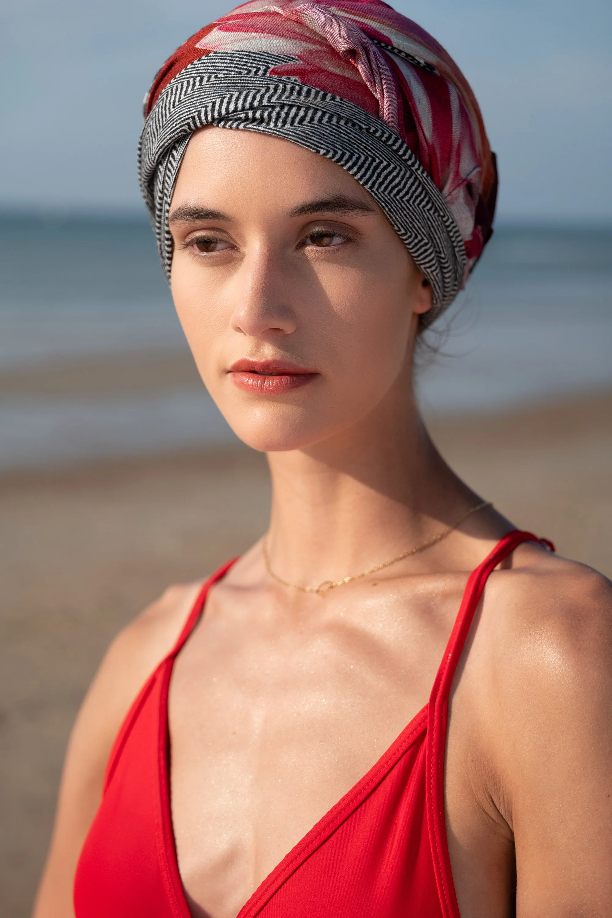 A woman wearing a colorful headscarf and a red swimsuit standing on the beach.