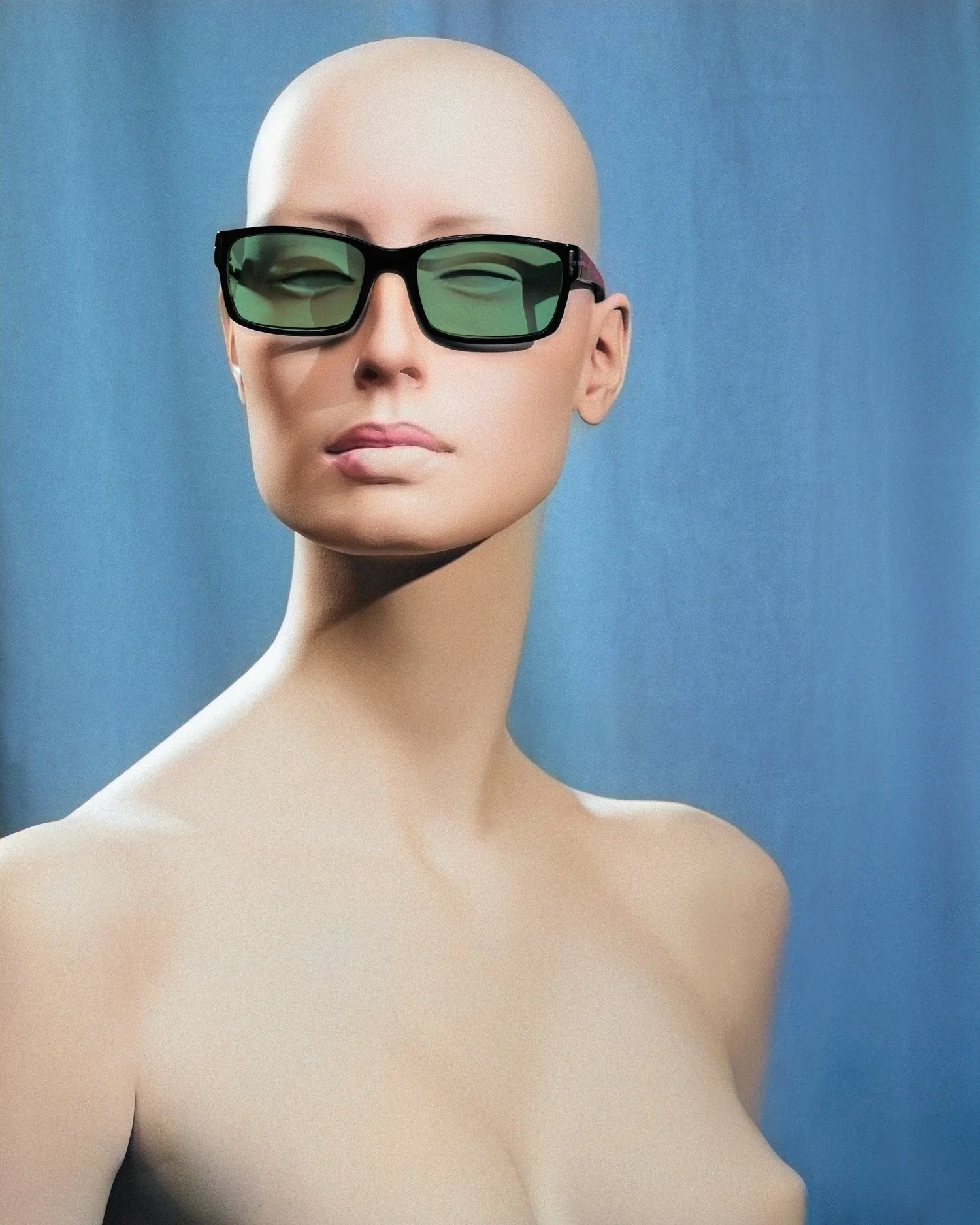 A mannequin with a bald head and fair skin wearing black sunglasses with green lenses against a blue background.