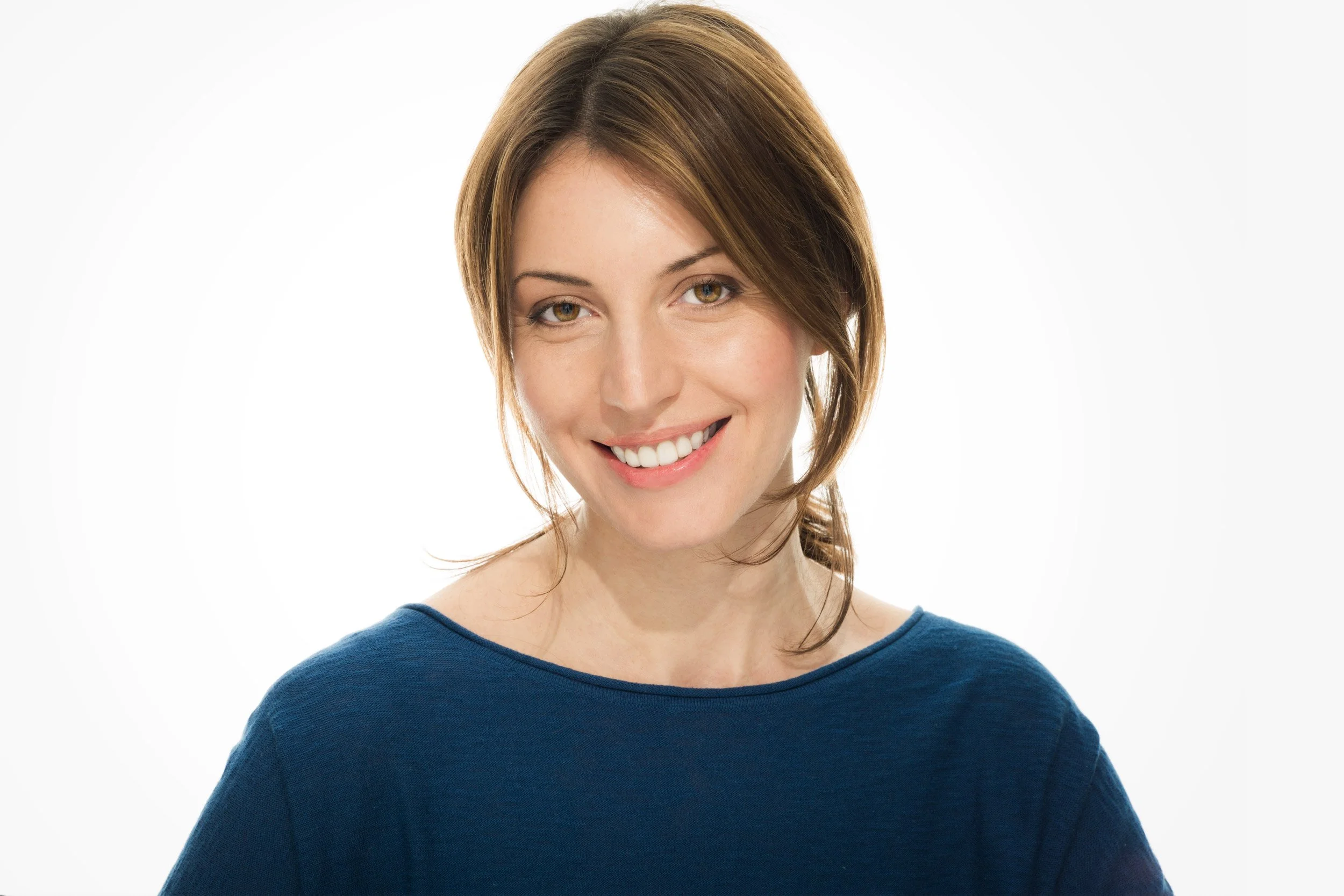 Smiling caucasian woman with pulled-back brown hair and boat-neck top photographed in J Heroun's signature headshot lighting style featuring open, defined shadows. Shot against a pure white background.