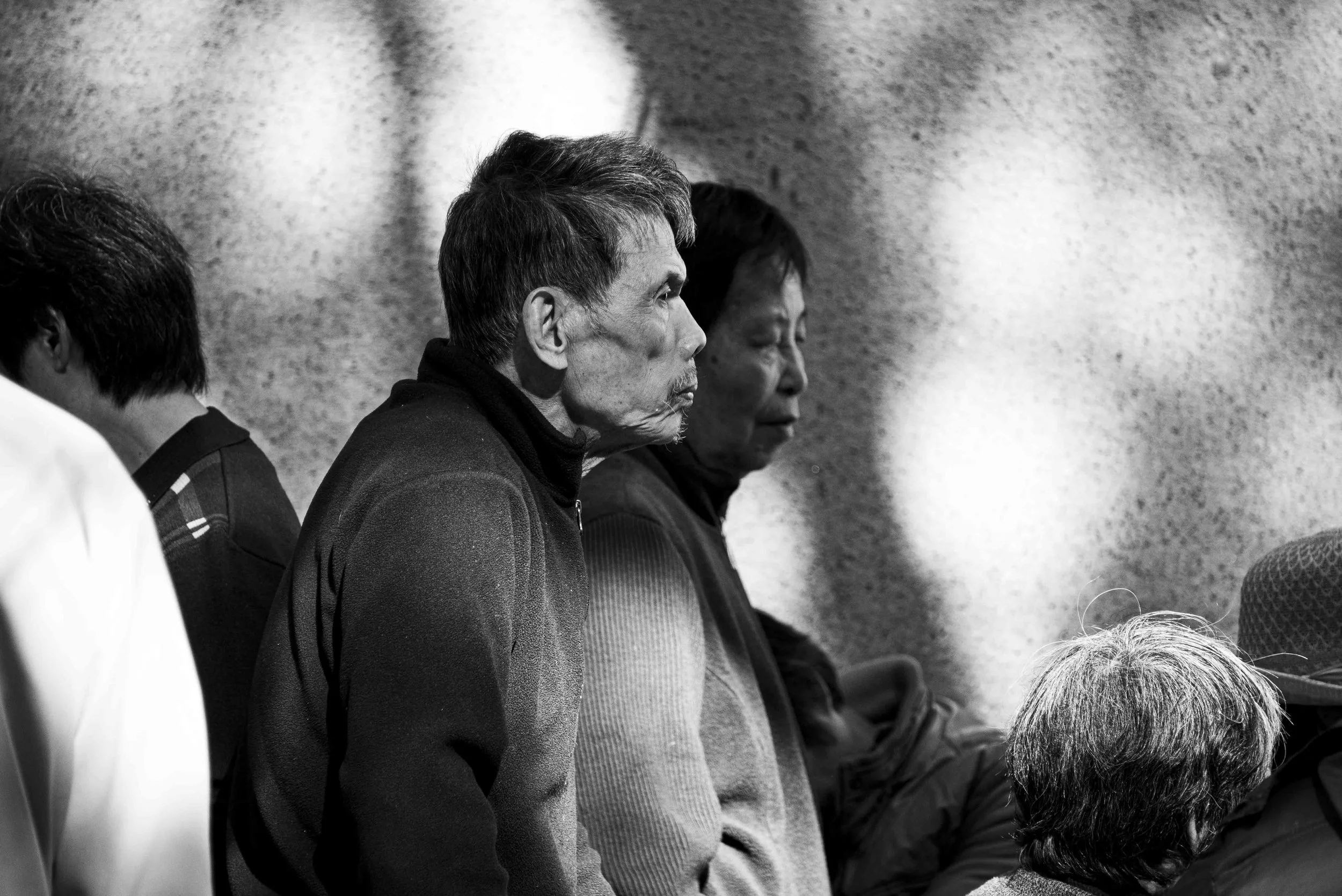 Black and white photo of people sitting with heads bowed, eyes closed, in prayer or meditation against a textured wall.