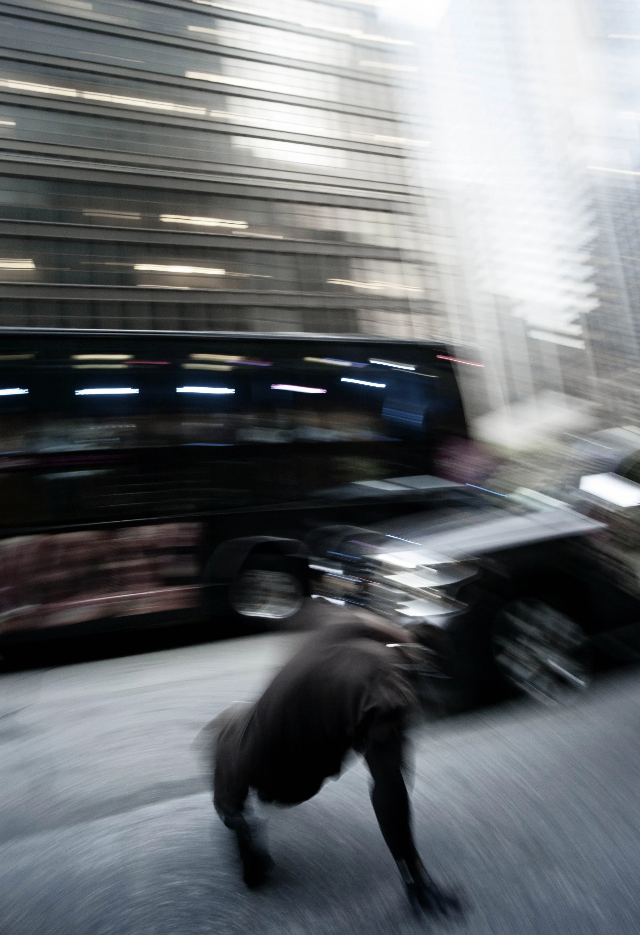 Person falling or crouching on a city street, with tall glass buildings in the background and motion blur effect.