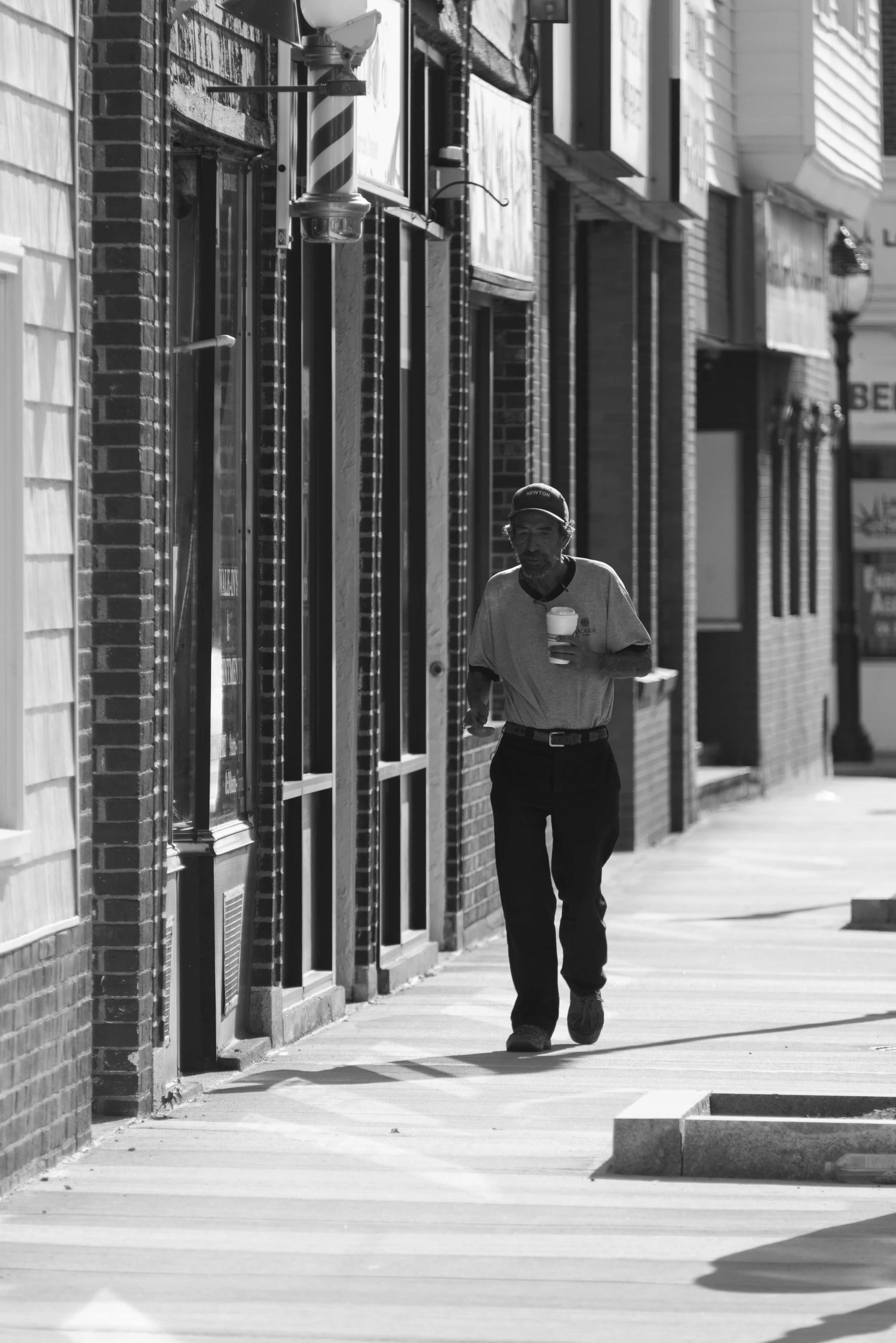 A man with a beard and cap walking on a city sidewalk, holding a coffee cup.