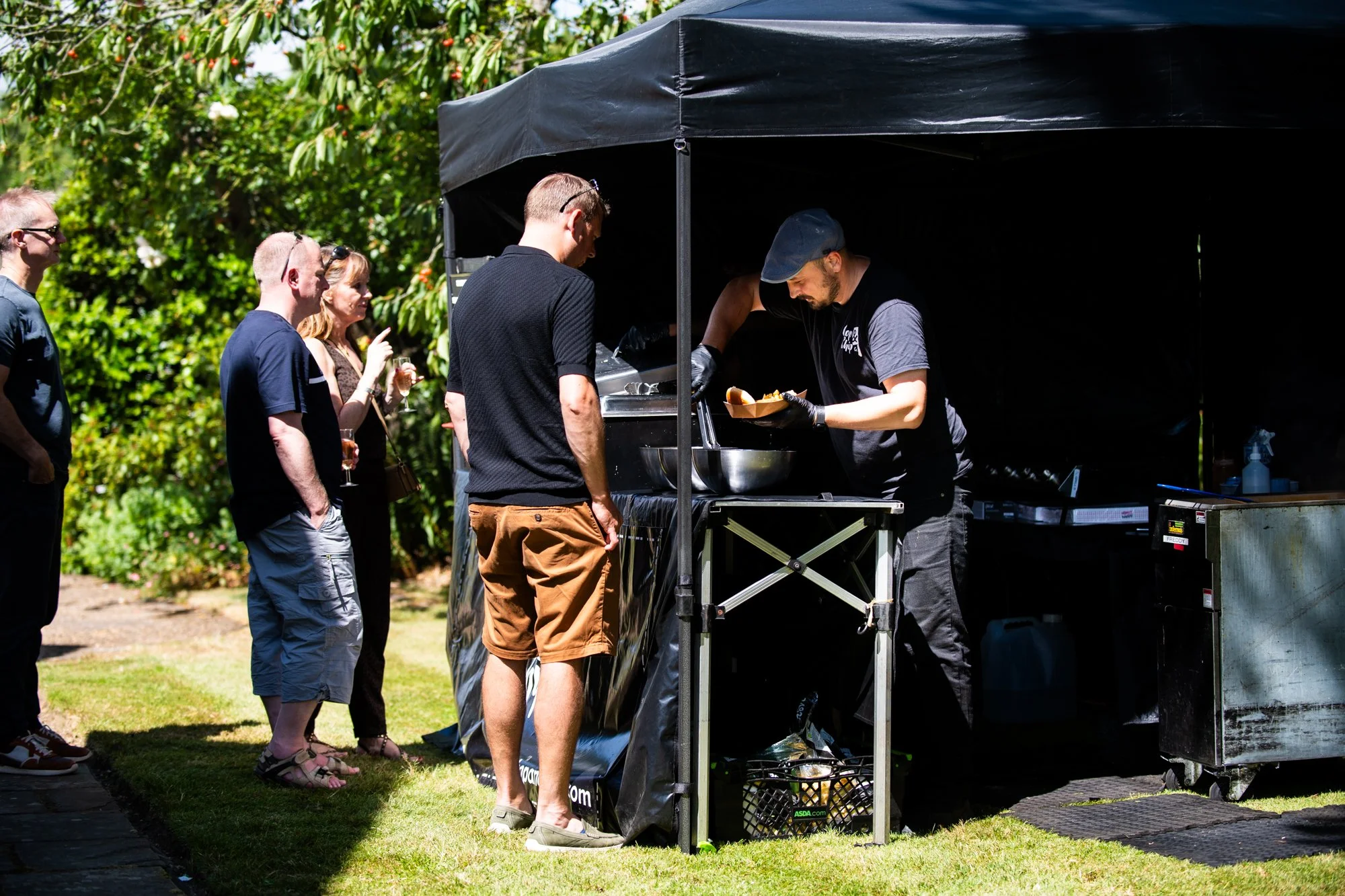 People standing in line at a food truck ordering food from a chef preparing meals outdoors.