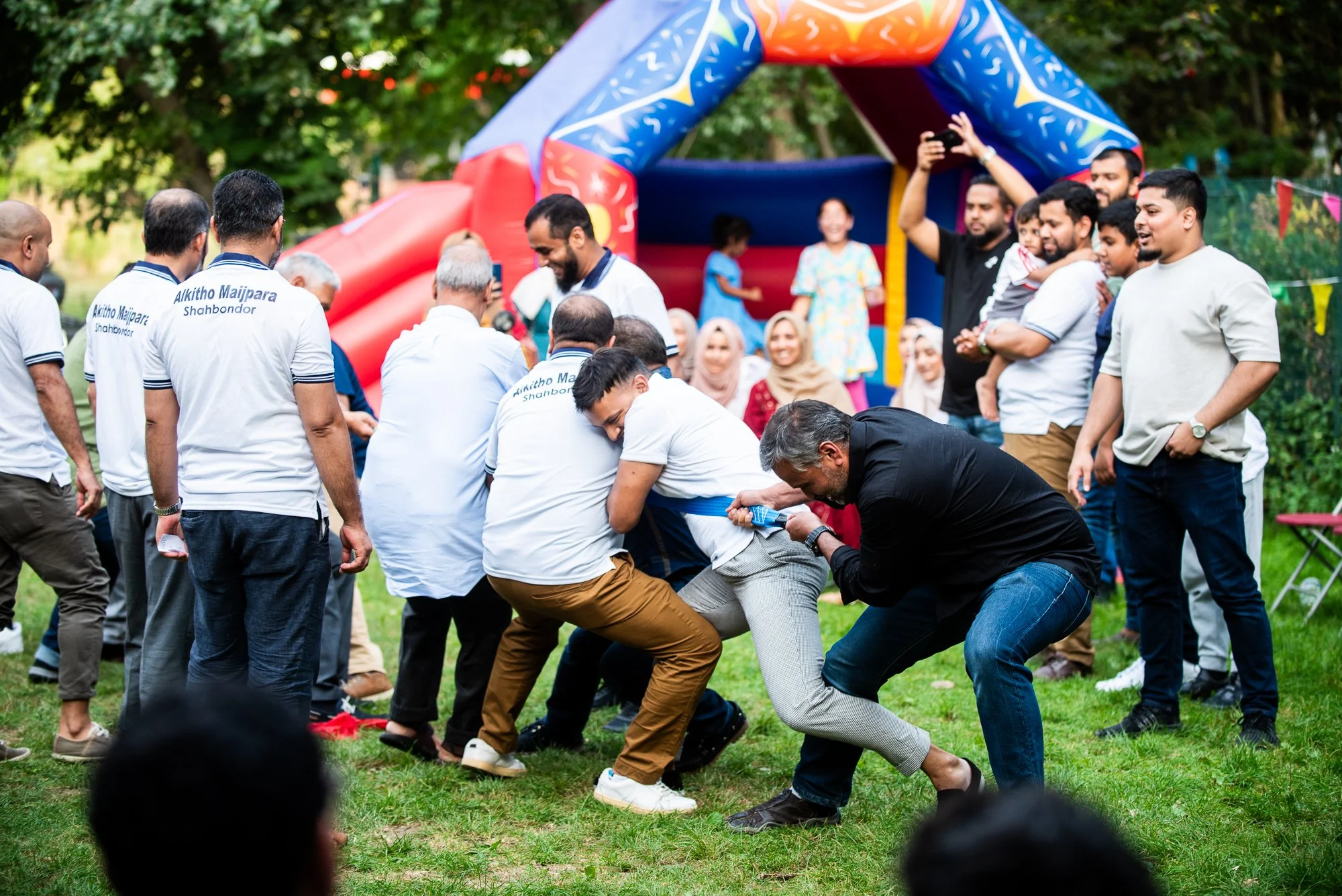 People participating in a tug-of-war game outdoors at a festive event with a bounce house in the background.
