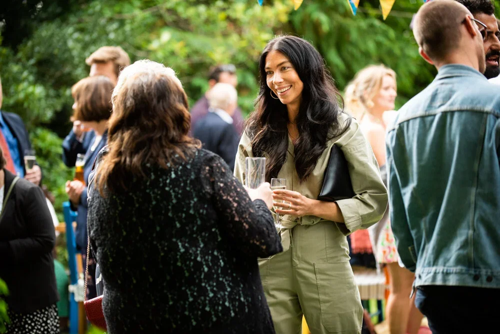People socializing at an outdoor gathering, with a woman smiling and holding a glass of drink, surrounded by others in casual attire.