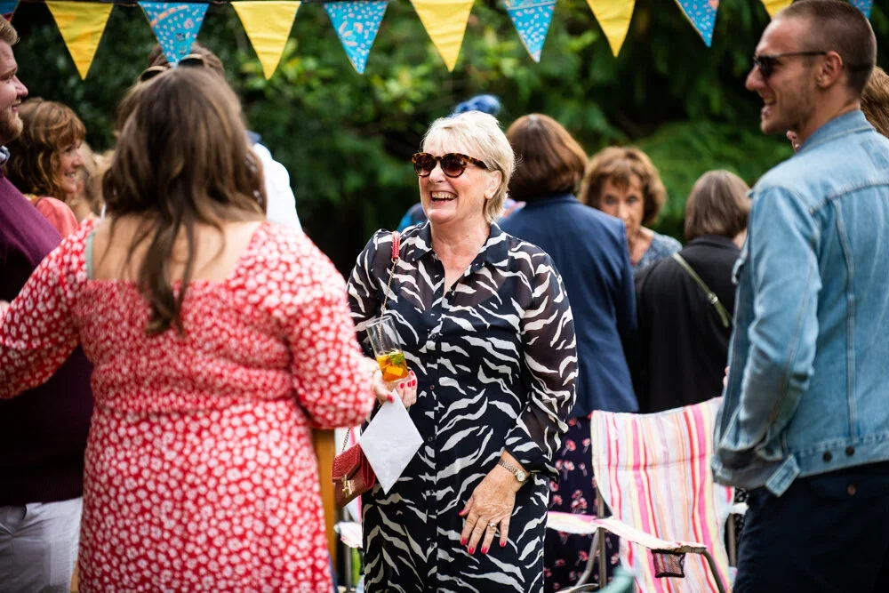 A group of people enjoying an outdoor social gathering with colorful bunting, smiling, and chatting.
