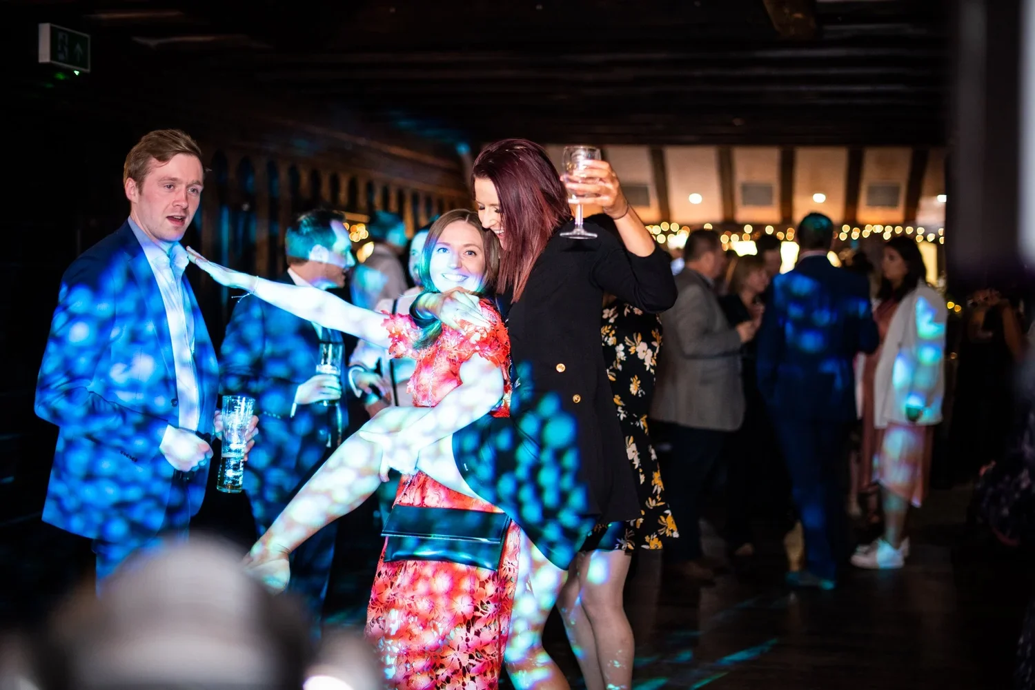 People dancing and socializing at a party with colorful lighting.