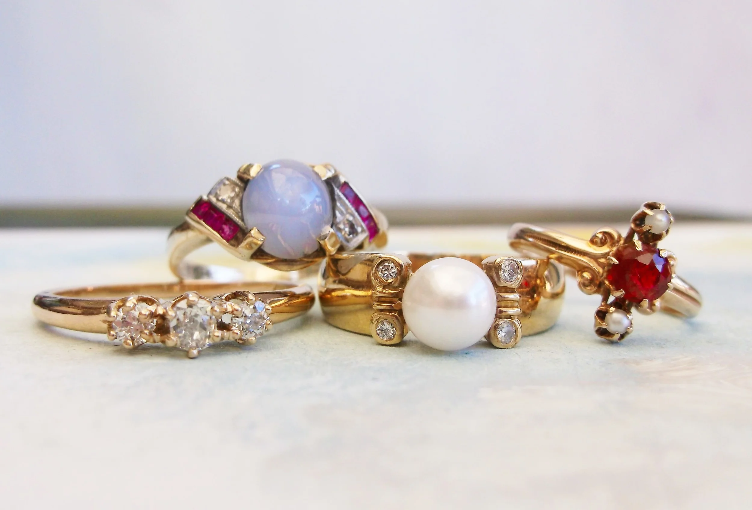 From Left to Right: *SOLD - Three stone Old Mine cut diamond ring with 0.25 carats total weight in diamonds set in 14K yellow gold. *SOLD - Retro star sapphire, ruby and diamond ring set in 10K yellow gold. *SOLD - 18K yellow gold, pearl and diamond ring. ... *SOLD - Victorian pearl and garnet doublet ring set in 14K yellow gold.