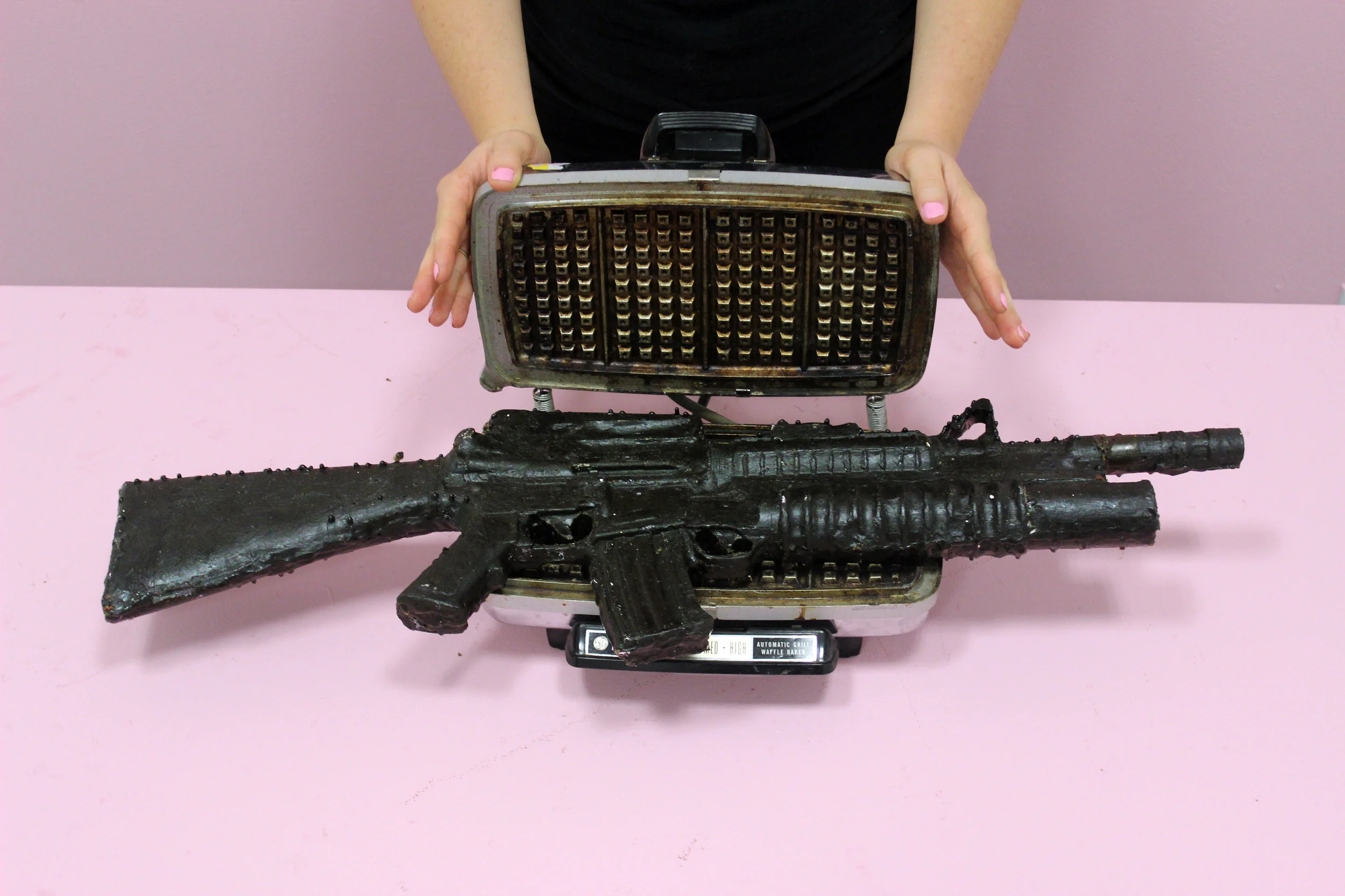   Title:&nbsp; To(get)her: Meeting/Melting/Mending,&nbsp;Gun/Nails/Waffle Iron  Media:&nbsp; Cast wax assault rifle, found waffle iron, "Pink Blink" nail polish  Size:&nbsp; 28" x 12" x 12"  Date:&nbsp; 2015 
