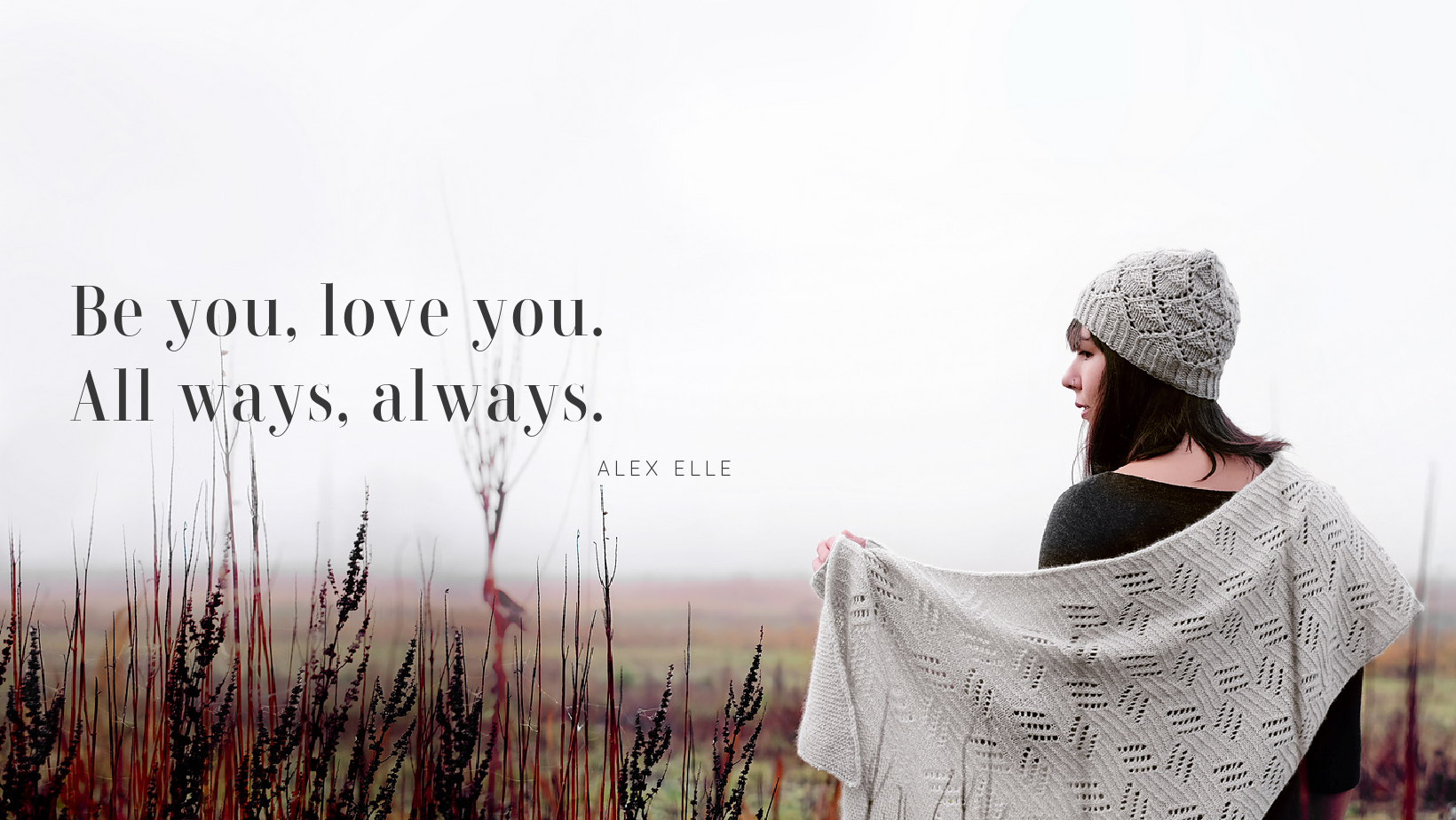 Dark haired woman wearing a hand knit shawl, hat and mitts in foggy field.