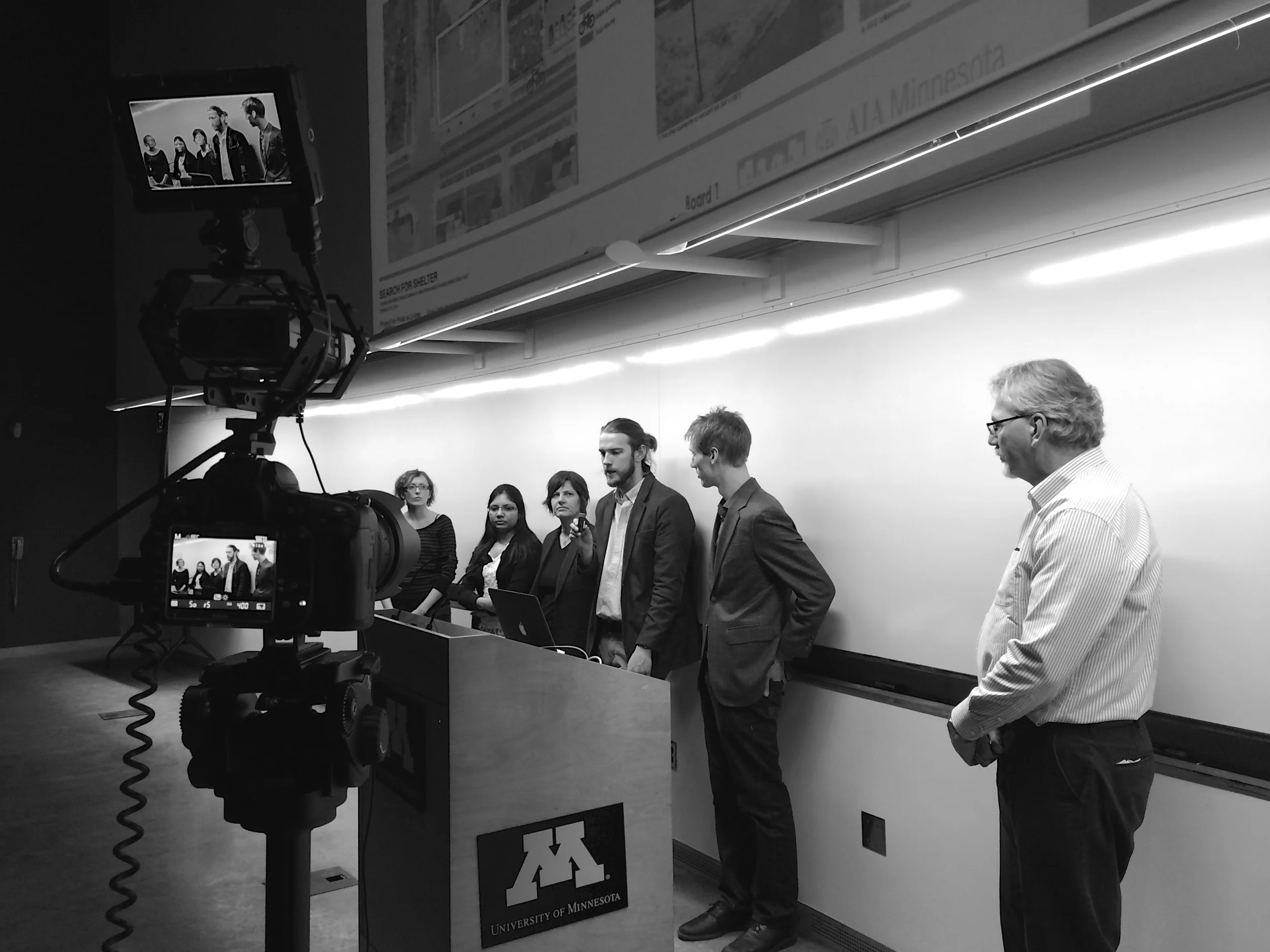 Charrette Team presenting their solution while being filmed from the "wings" of the stage.