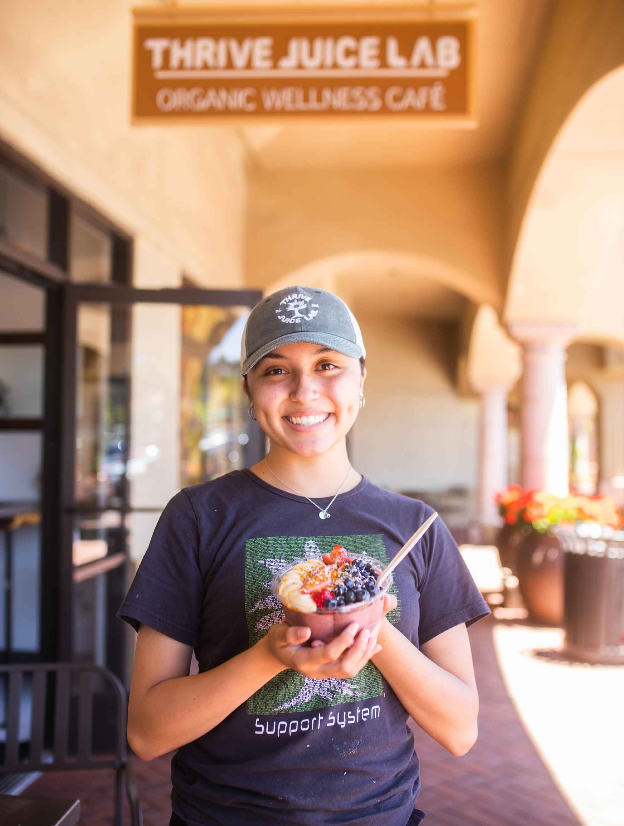  Thrive Juice Lab employee holding Acai Bowl with spoon in front of the store. 