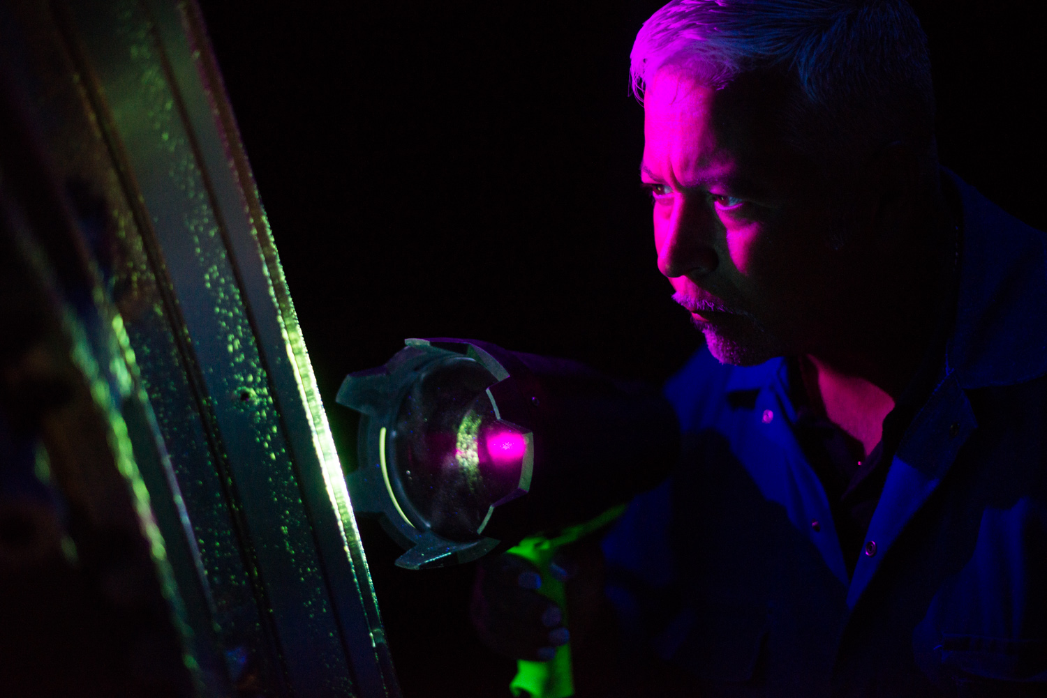 For this image, in an incredibly dark spray booth, I needed both to have some light on the engineer's face, but balanced with the very dim green light as the sprayed on agent glowed from his ultraviolet torch. My flashes and even my torch were far too bright, so I put a piece of purple gel over the torch on my iphone, and had my assistant hold it!