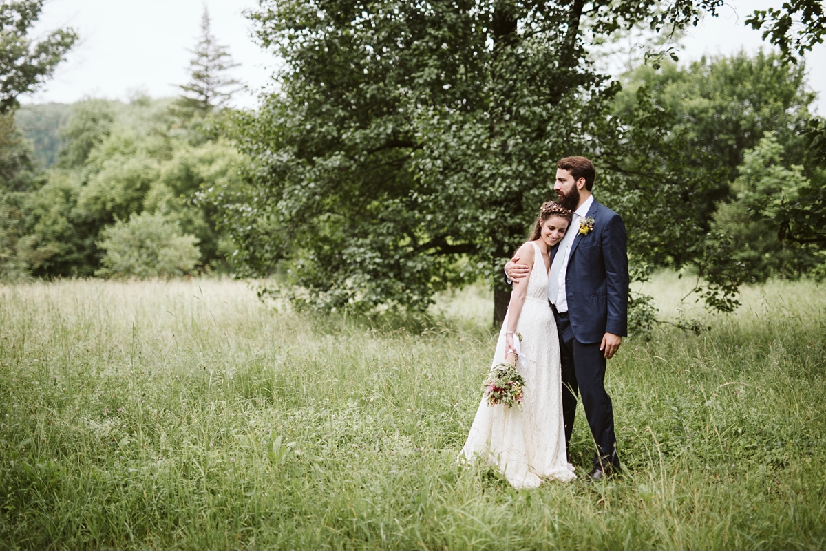 Bride leaning head on grooms chest in field during summer wedding