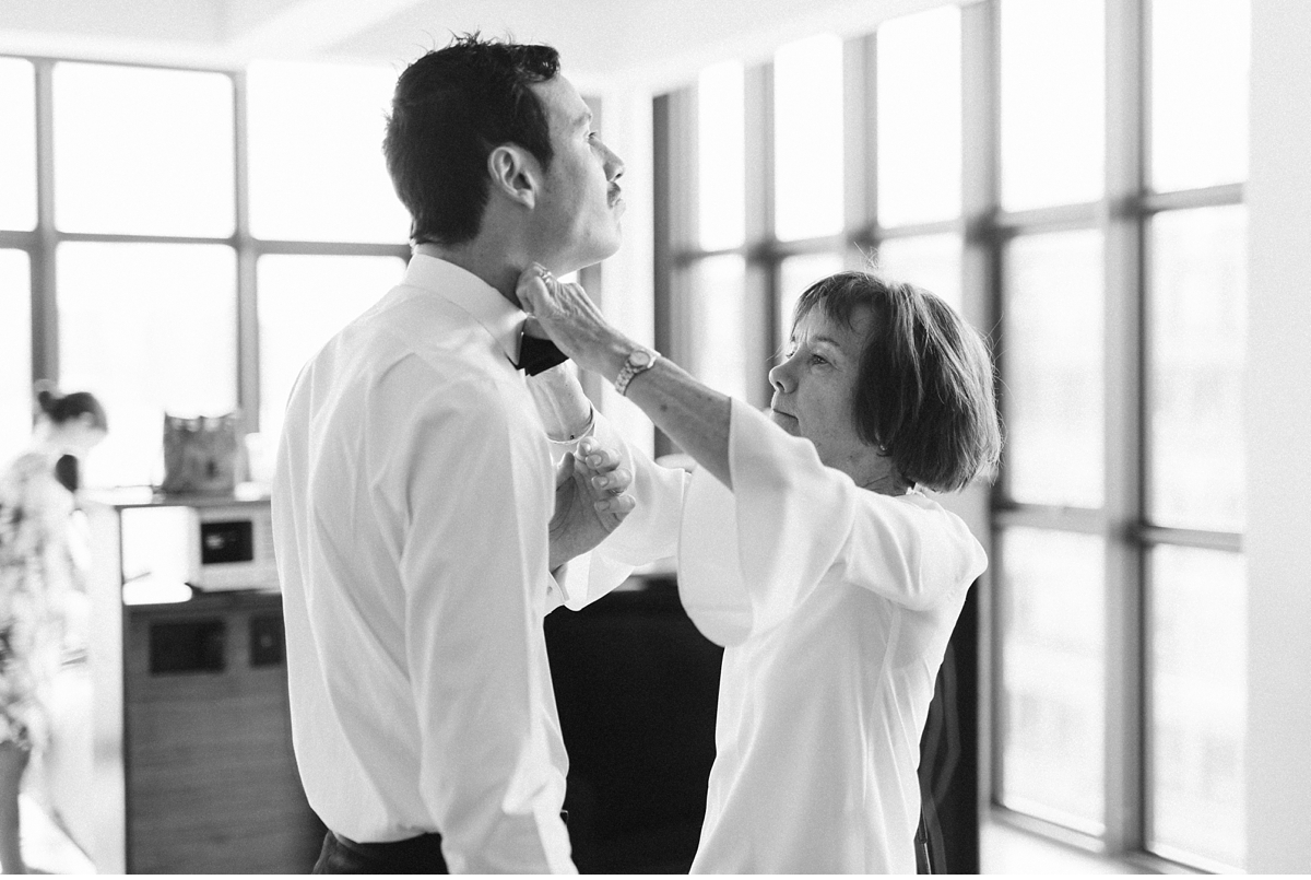 groom laughing while being helped with his bow tie