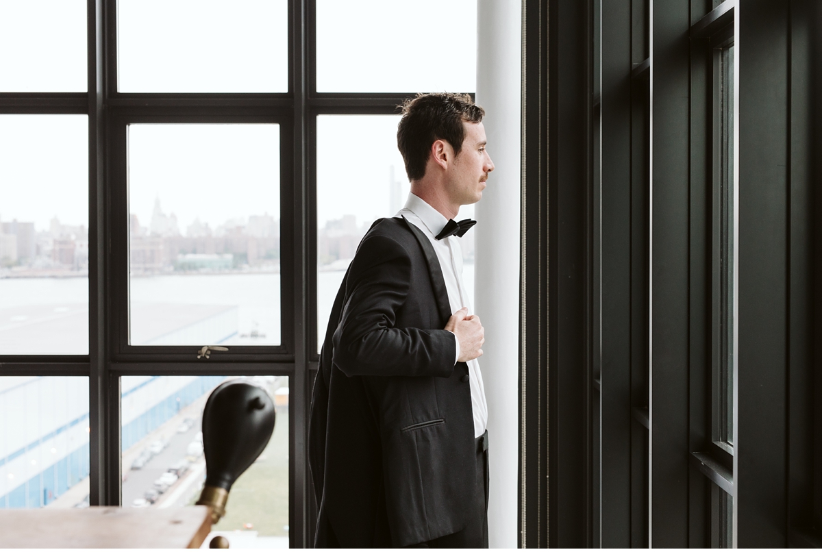 Groom putting on his jacket in front of large industrial window