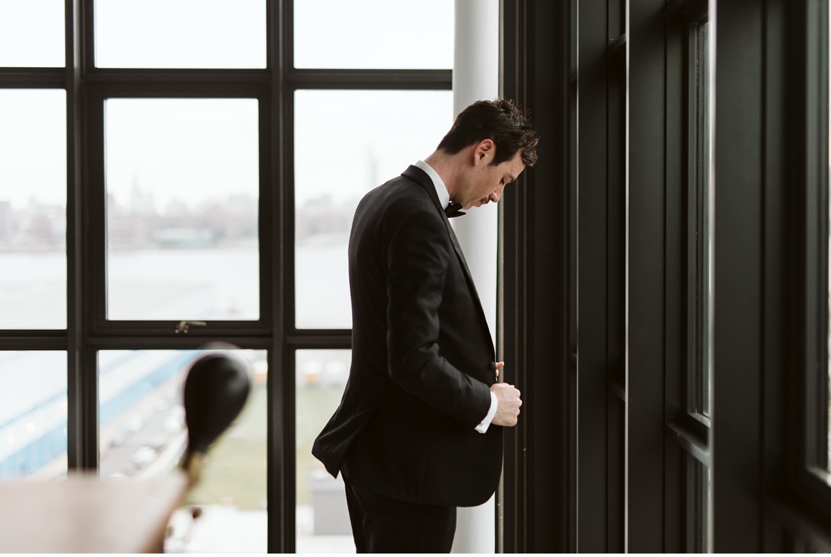 Groom buttoning his jacket in front of large window at the Wythe Hotel