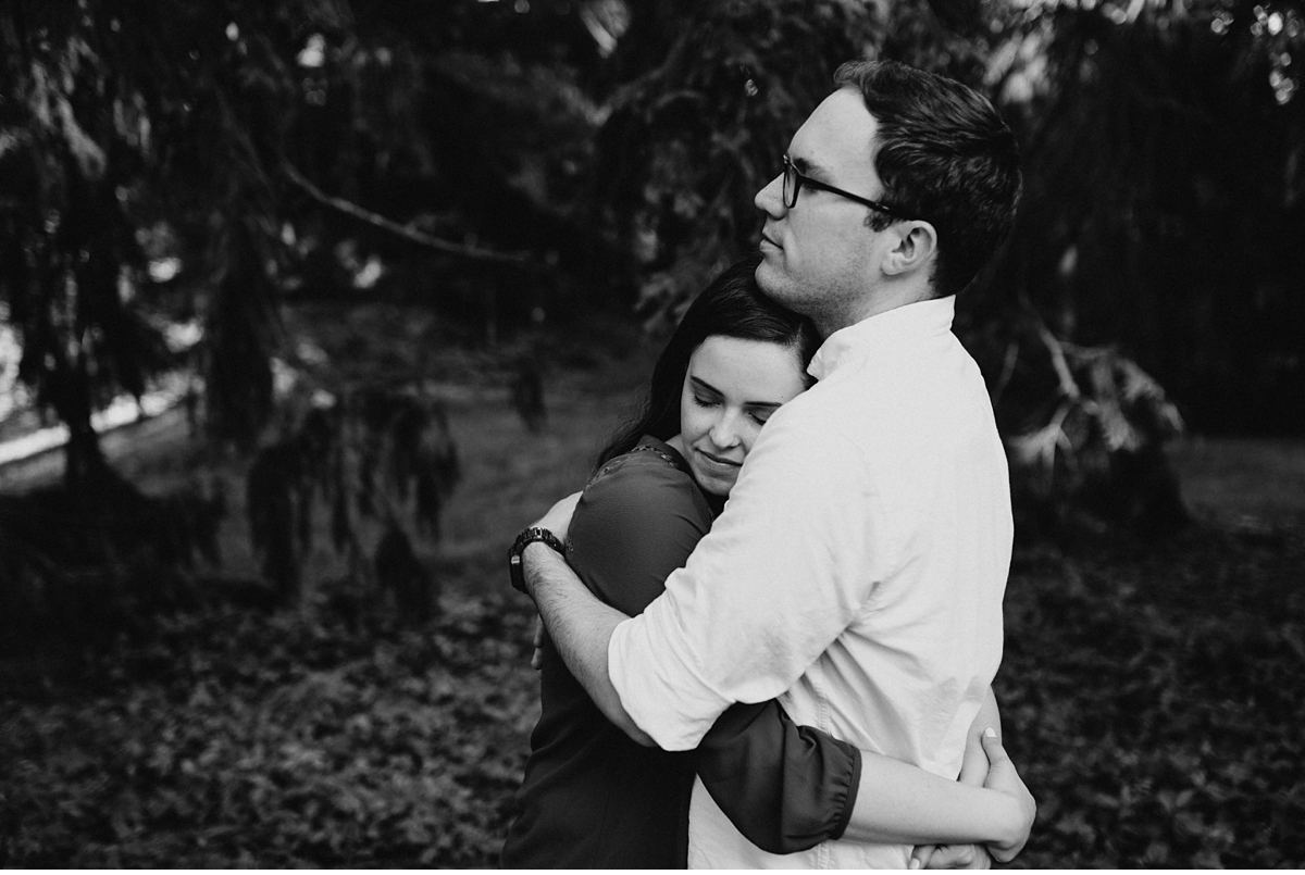 couple hugging surrounded by pine trees in the Arnold Arboretum in black and white
