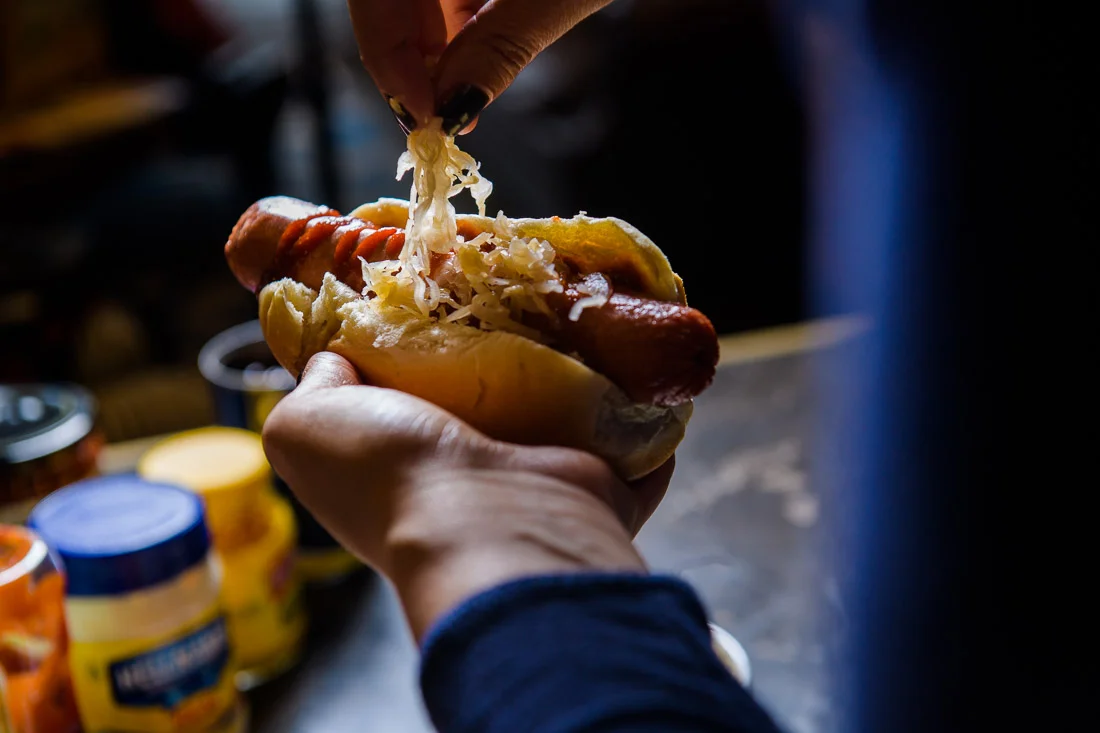 Branded Lifestyle Portrait chef author Daina Falk adding kraut to hot dog