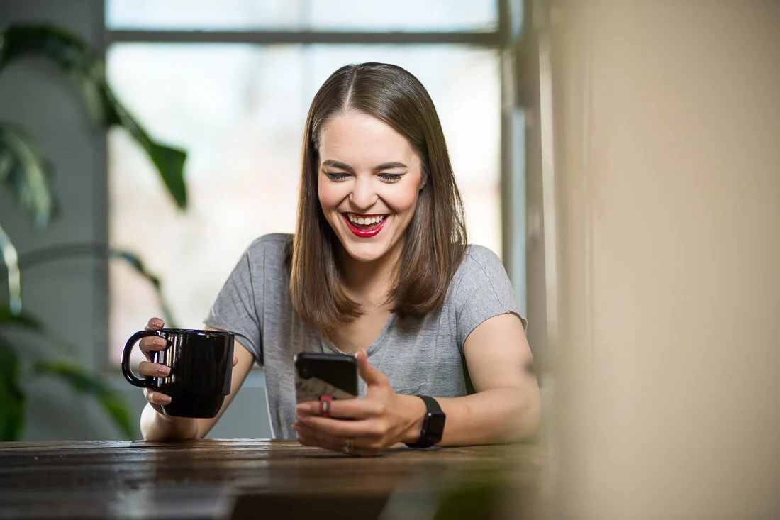 NYC personal branding photo Speaker Author Melanie Deziel working on her phone with coffee cup in other hand