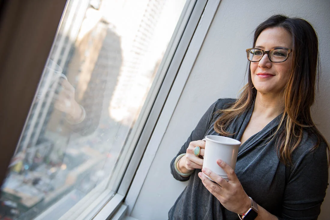 NYC branded lifestyle portraits speaker writer Terri Trespicio looking out window with coffee cup in hand